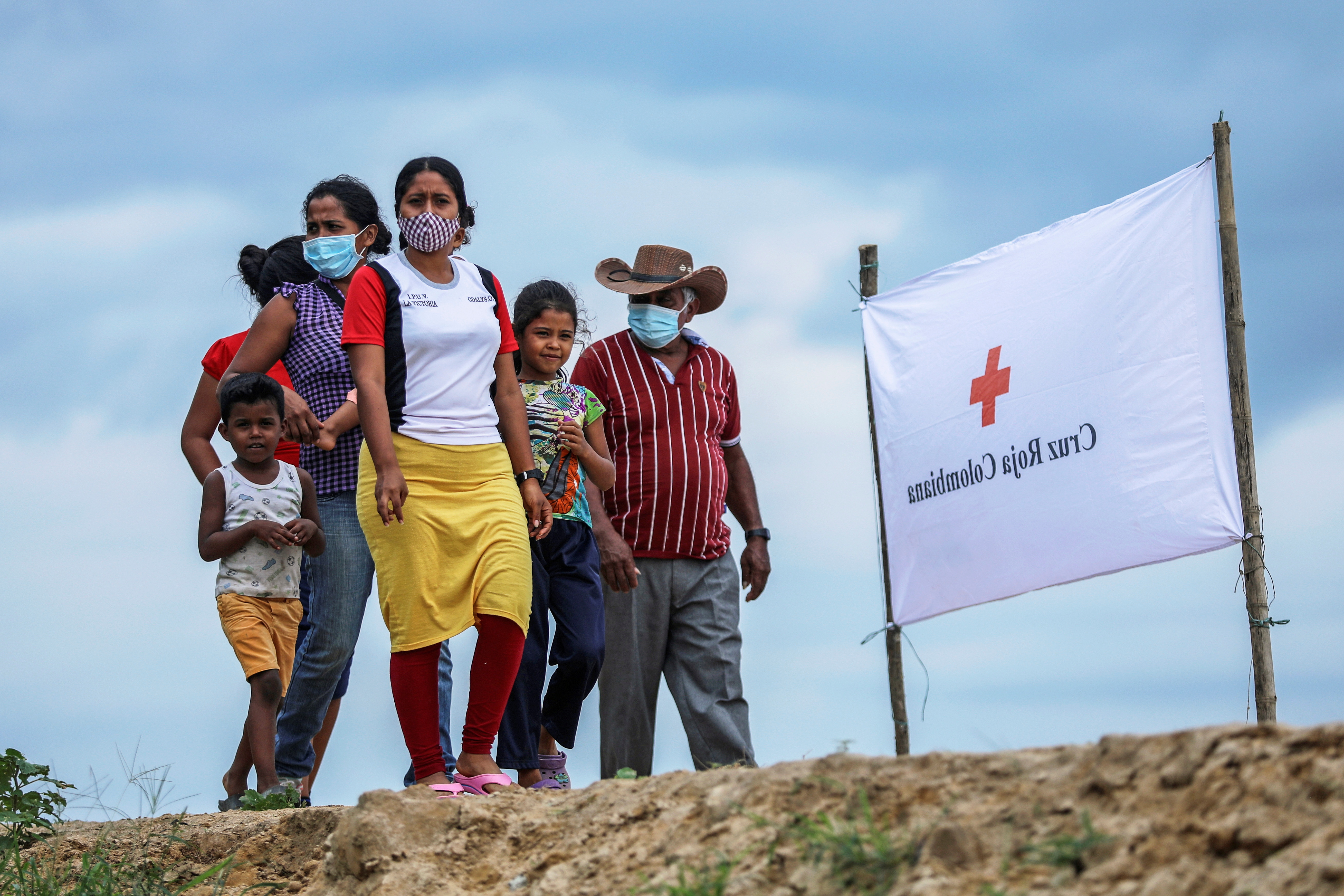 Venezuelan refugees stand in a group next to a white banner for the Red Cross.