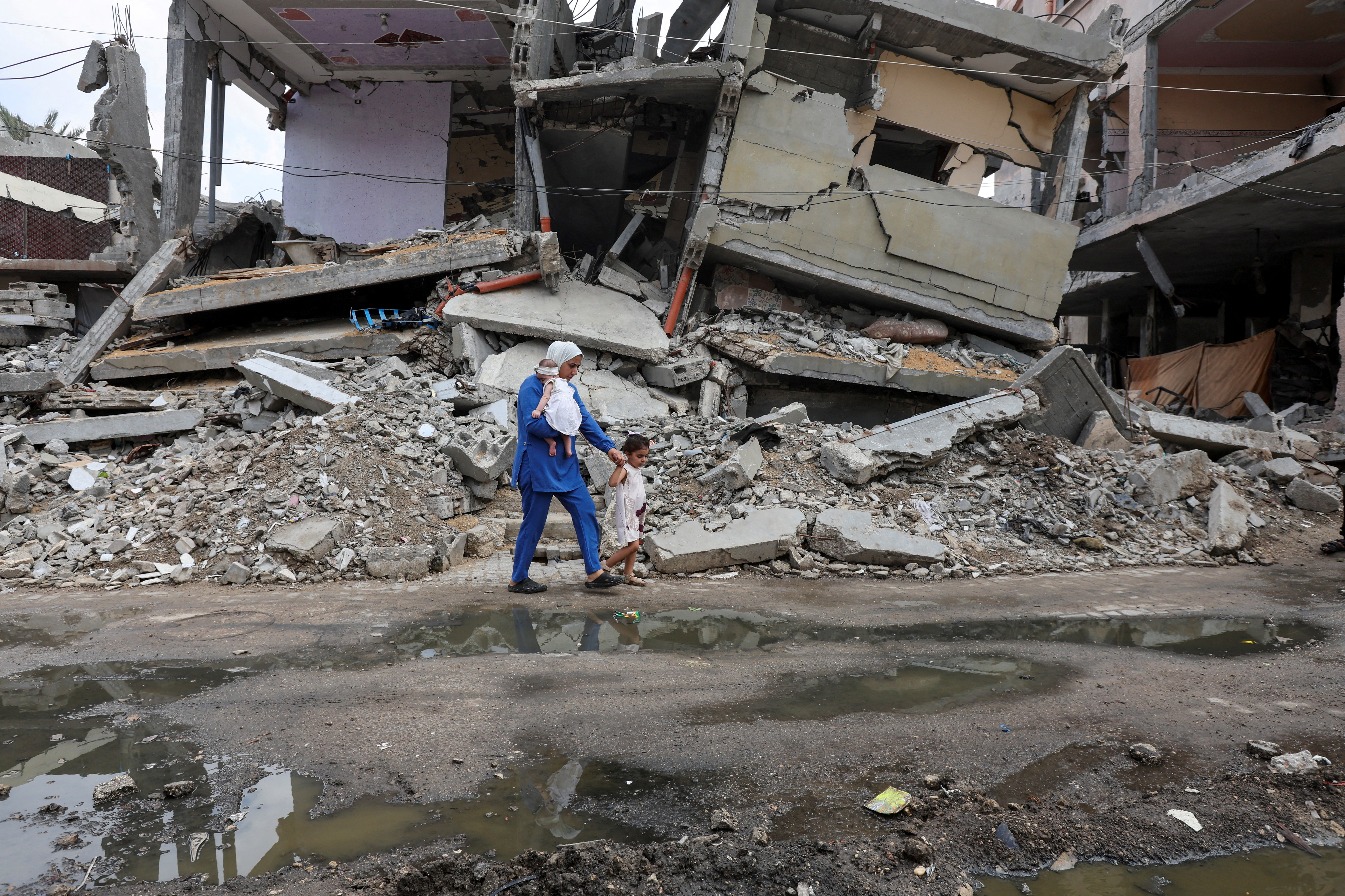 A displaced Palestinian mother, Wafaa Abdelhadi, walks past the rubble of a house destroyed in an Israeli strike as she returns to her shelter with her daughters Lynn and Roueida, after they got vaccinated against polio, in Deir Al-Balah, in the central Gaza Strip September 1, 2024. REUTERS/Ramadan Abed TPX IMAGES OF THE DAY