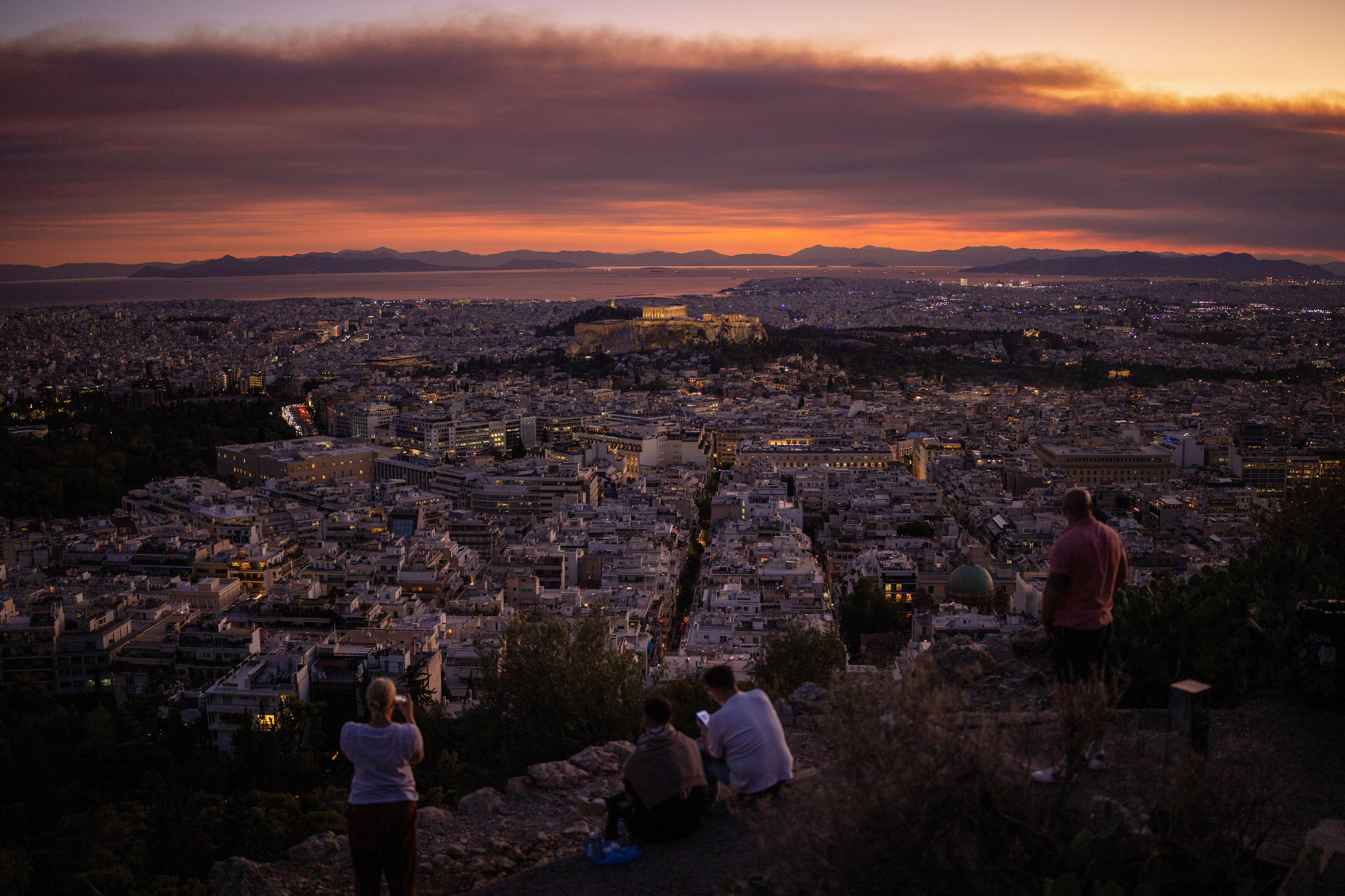 People enjoy the view with the Parthenon temple atop the Acropolis hill, as smoke from a wildfire burning in Corinth region blankets Athens
