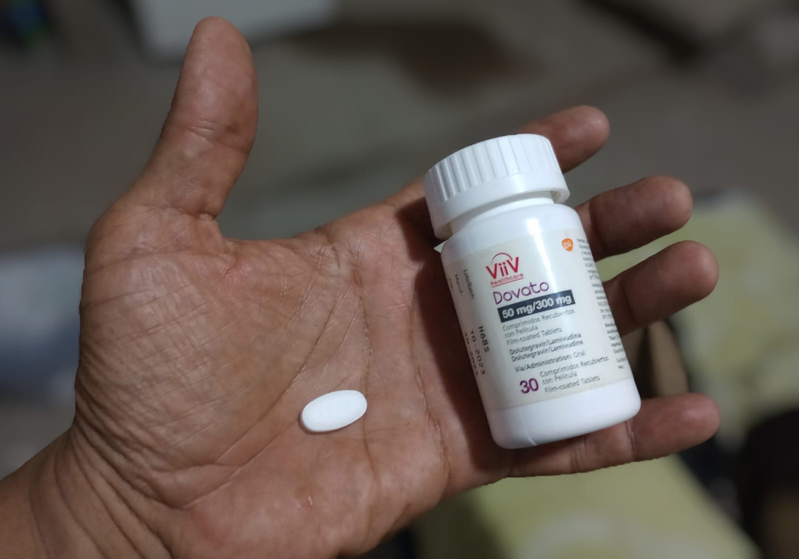 A hand stretches out to show a bottle of dolutegravir and a solitary pill resting in his palm.