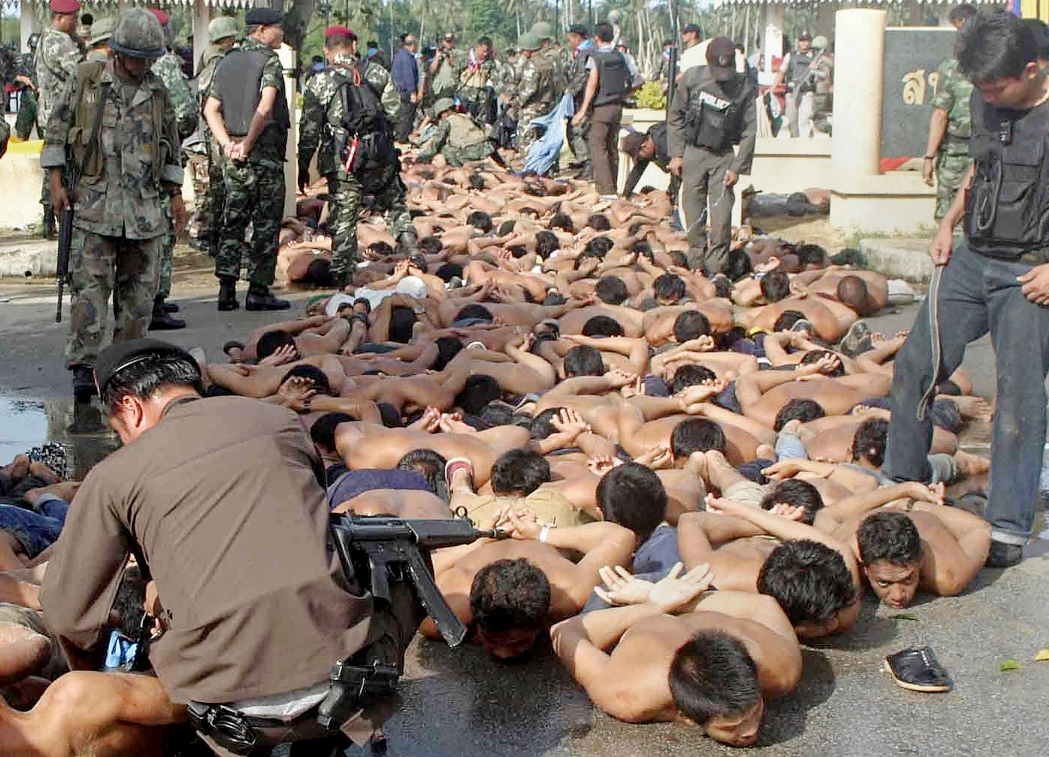 Protesters lying on the ground. Their hands have been tied behind their backs and they are bare chested. Thai soldiers and security personnel are watching them.