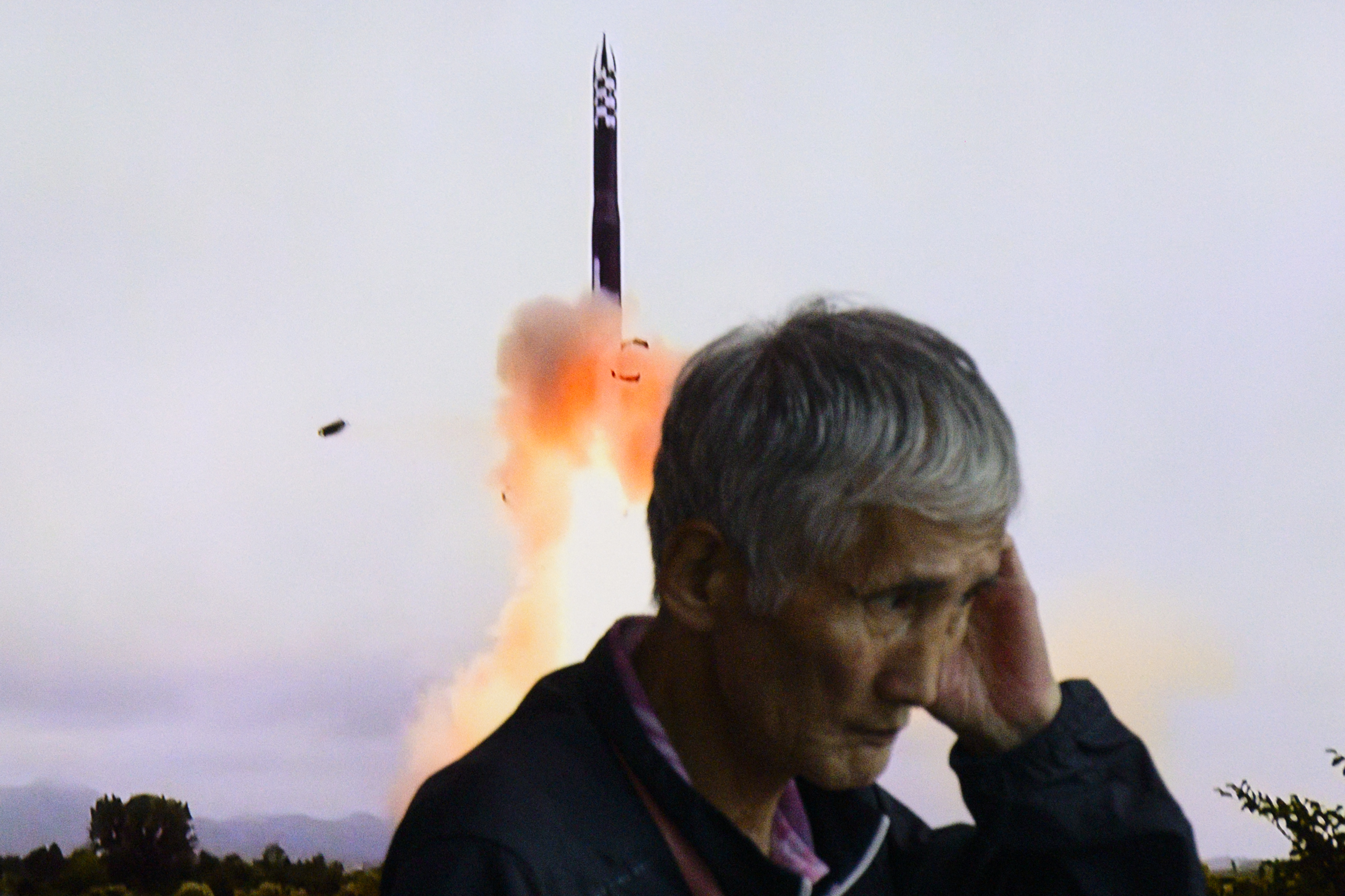 An elderly man in front of a large TV screen showing a missile launching into the air