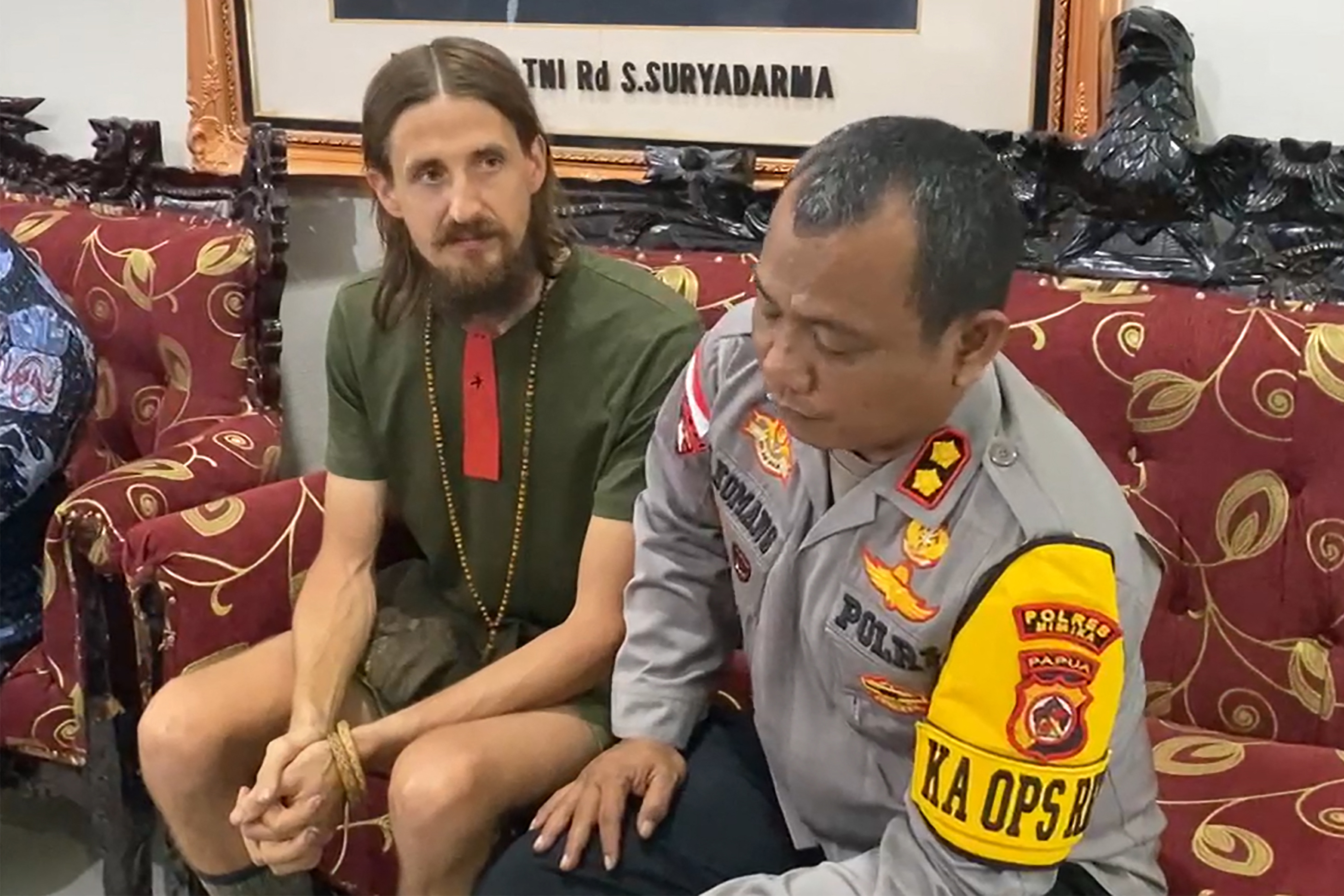 Phillip Hertens sitting with an Indonesian official. Merten looks thin but healthy. He has long dark hair and a beard.