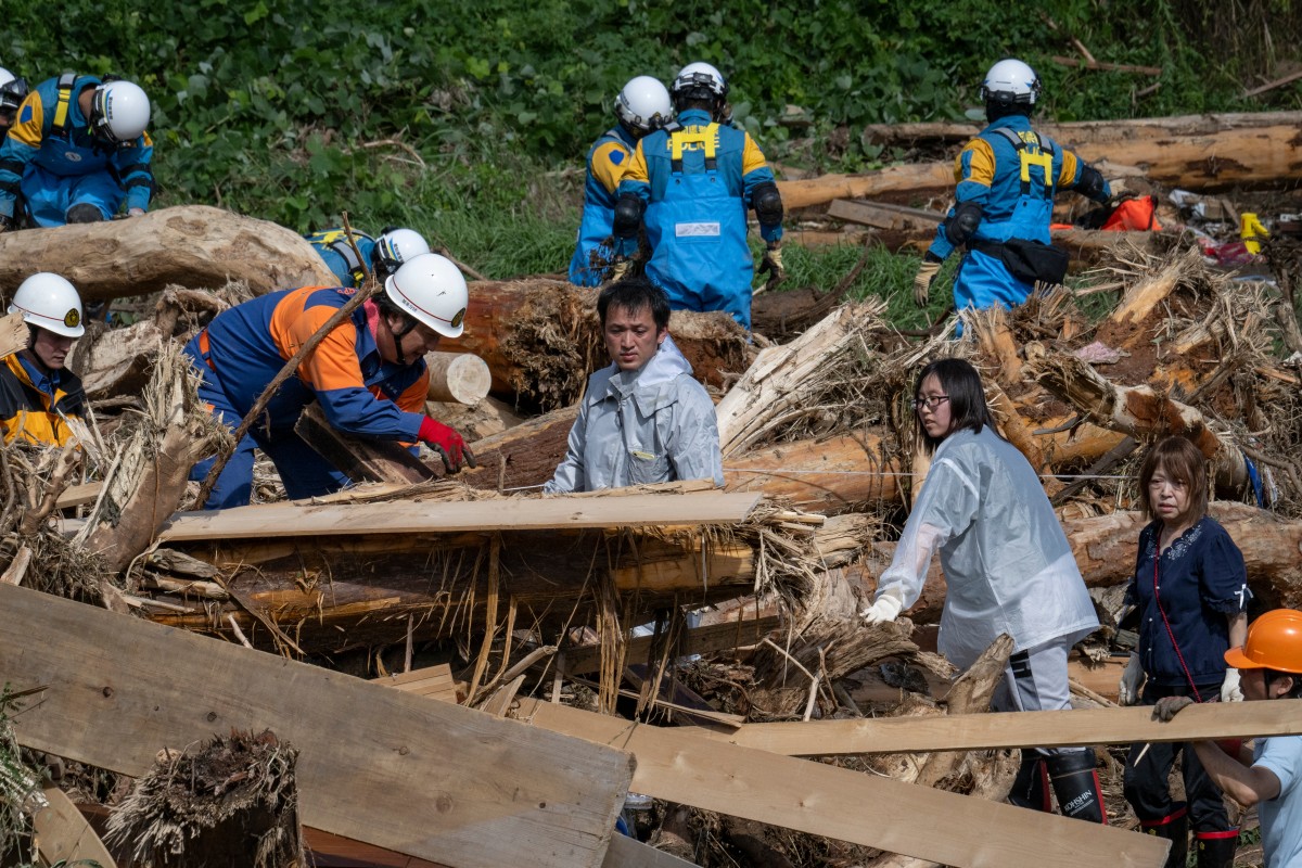 A father (C) searches for his missing 14-year-old daughter among debris washed away from flooding along the Tsukada river