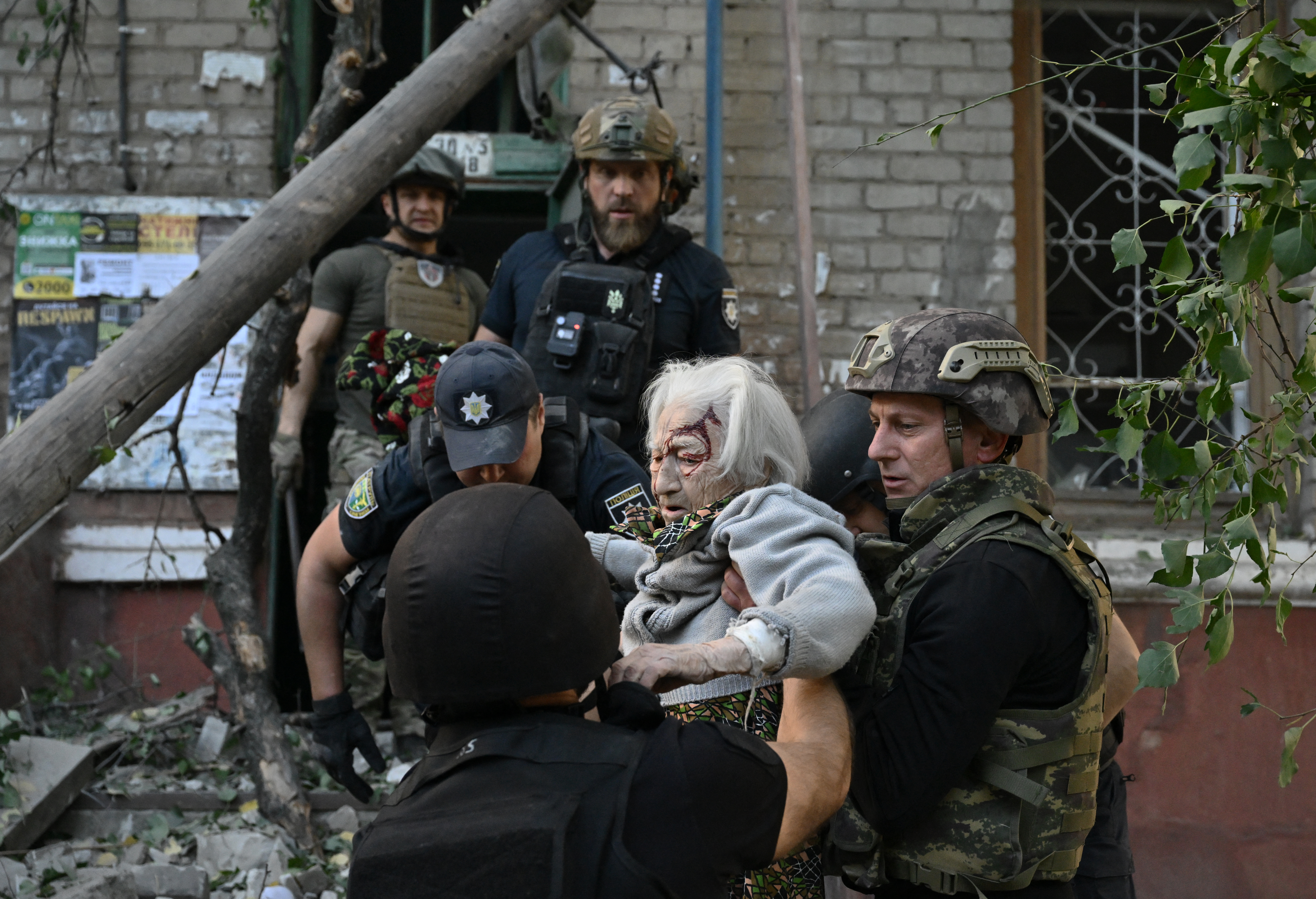 Rescuers helping an elderly woman after her apartment was hit by a Russian bomb. She has blood and dust on her face