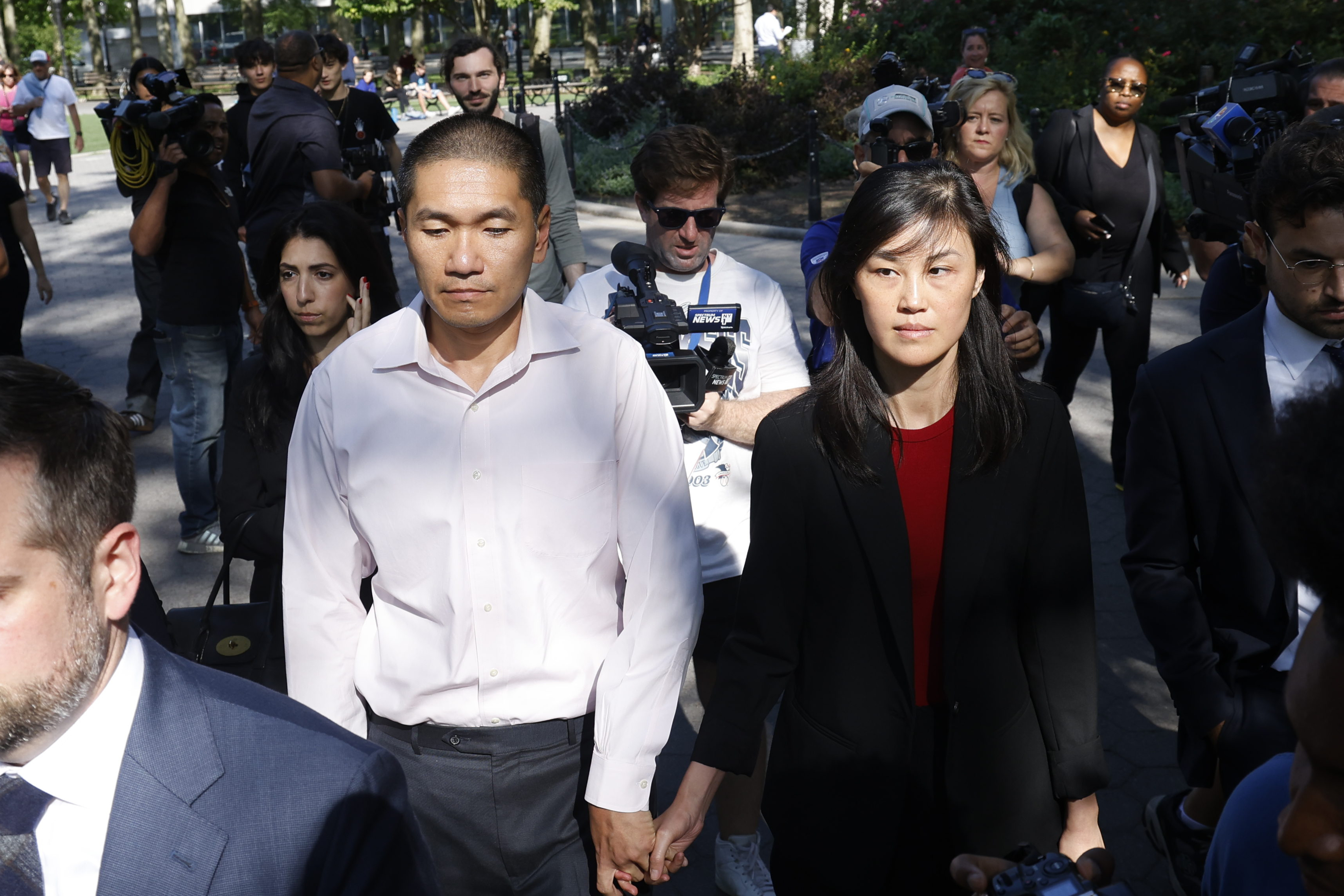 Linda Sun and her husband Christopher Sun walk outside a court, surrounded by press