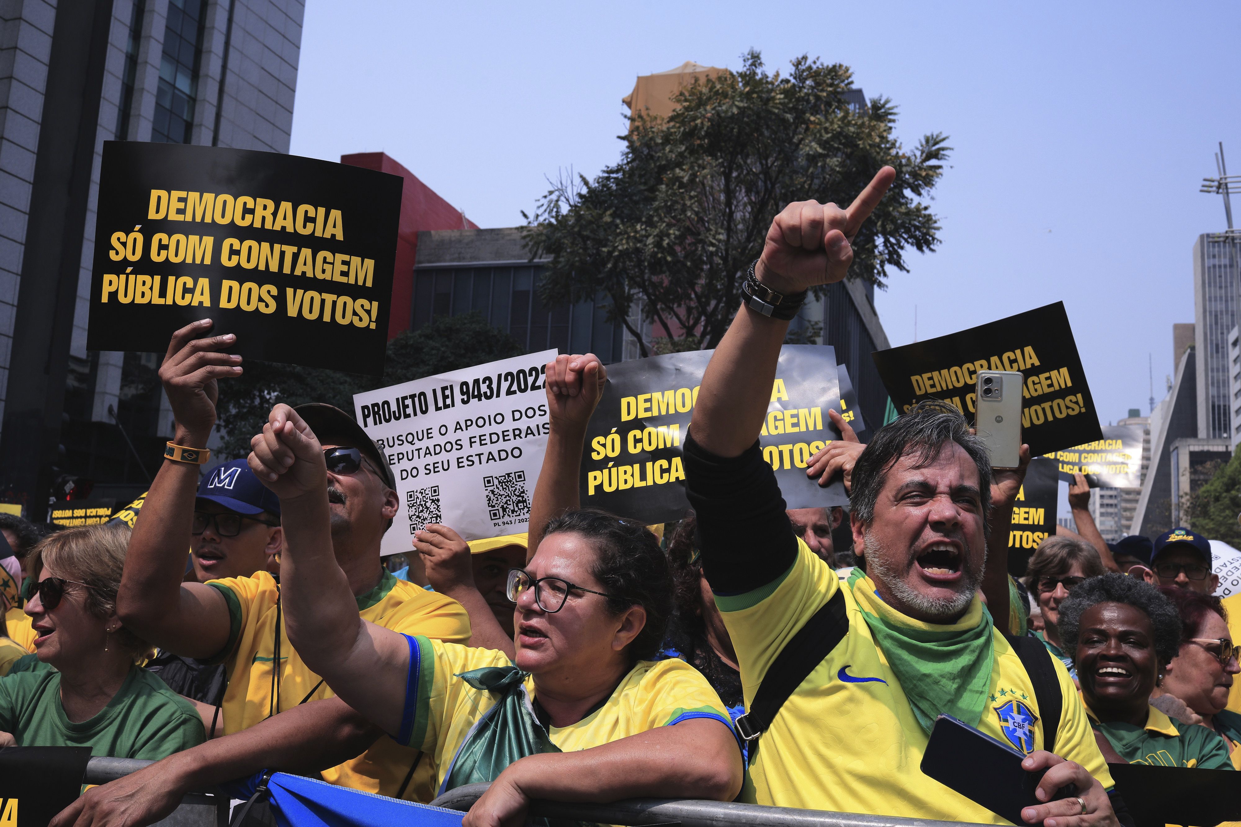 Protesters hold up signs and point fingers angrily into the air at a protest in Sao Paulo.