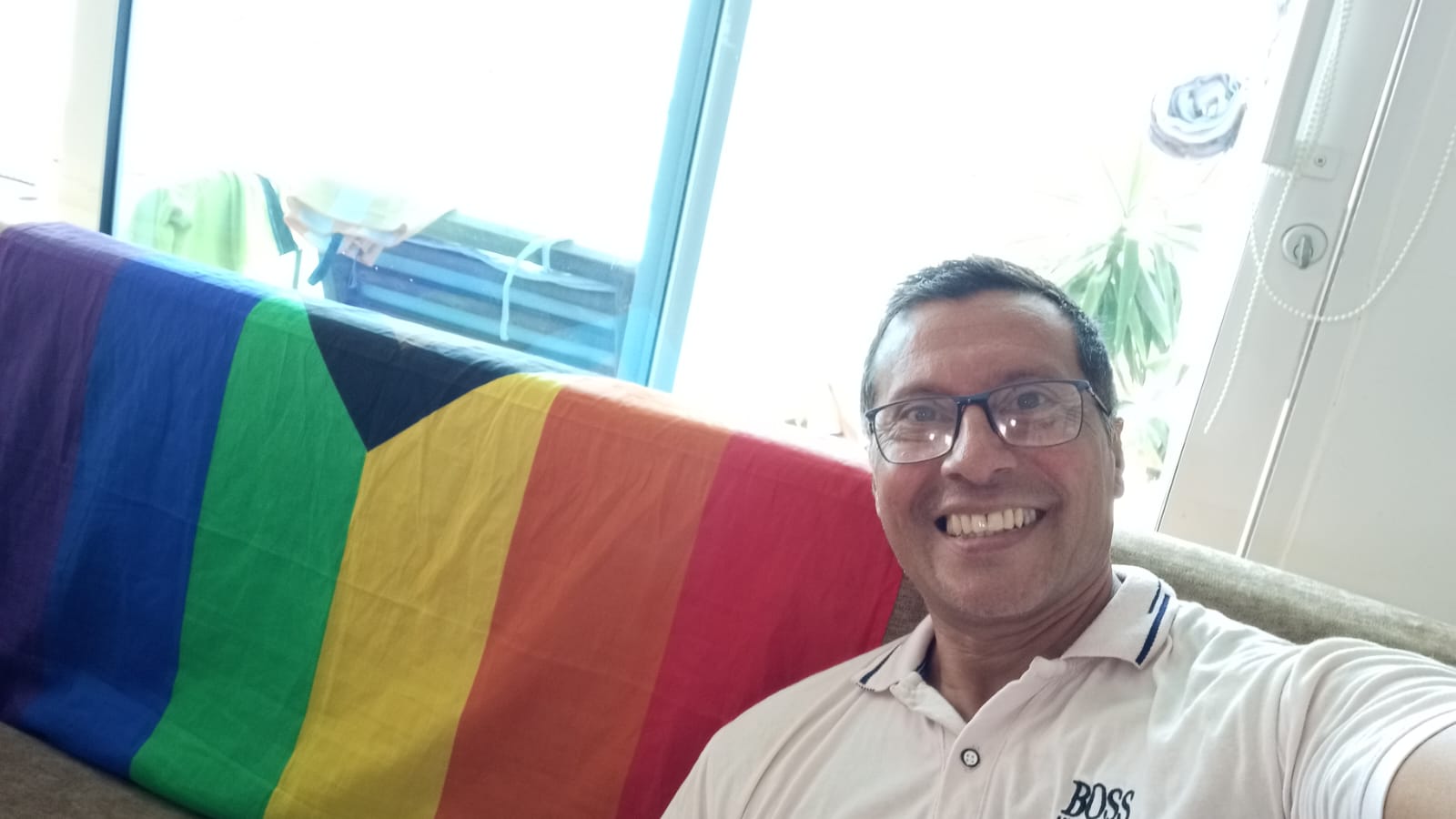 Ariel Villan takes a selfie next to a rainbow Pride flag.