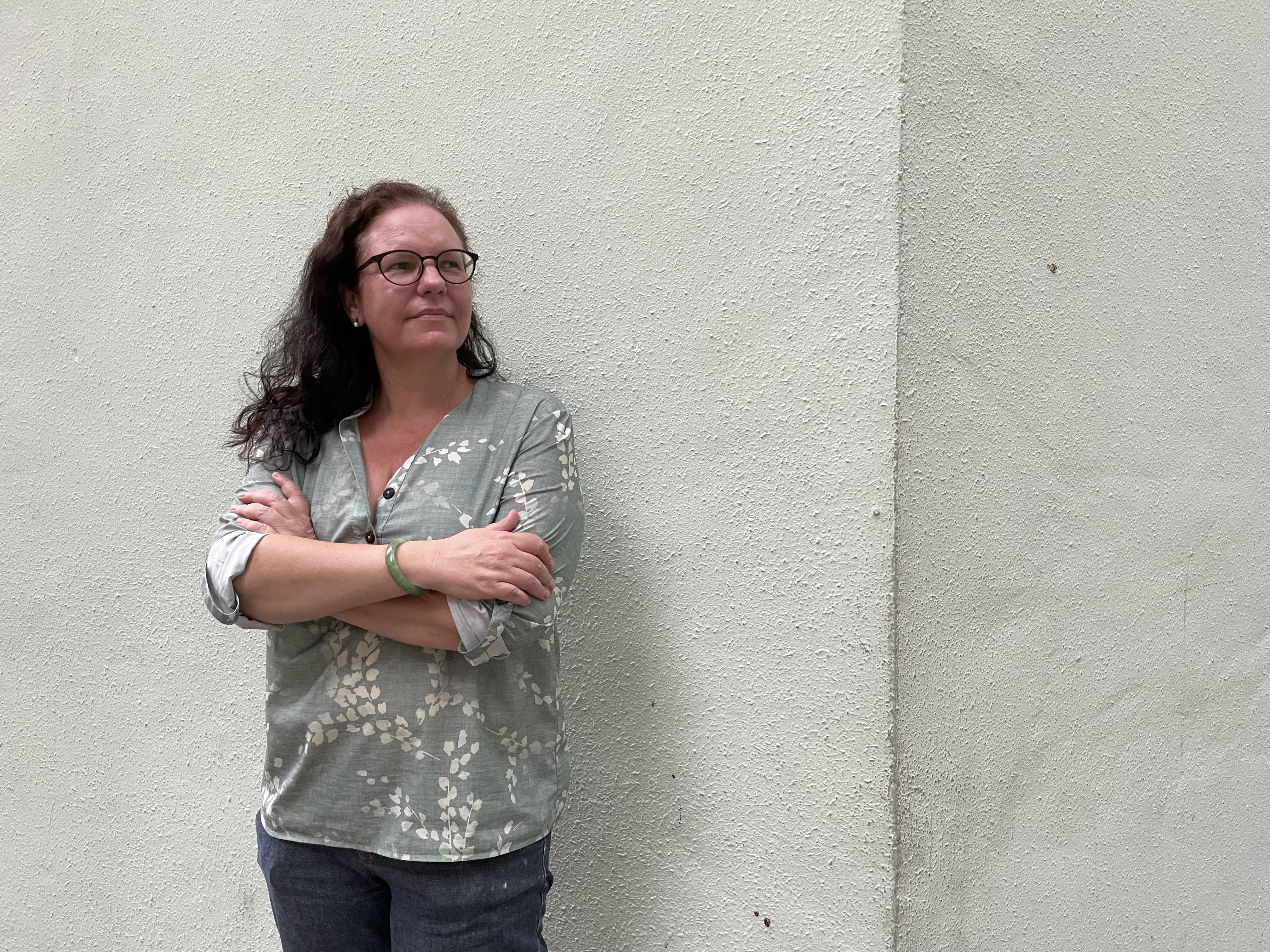 Chloe Martin. She has curly medium length hair and is wearing glasses. She is standing against a white wall