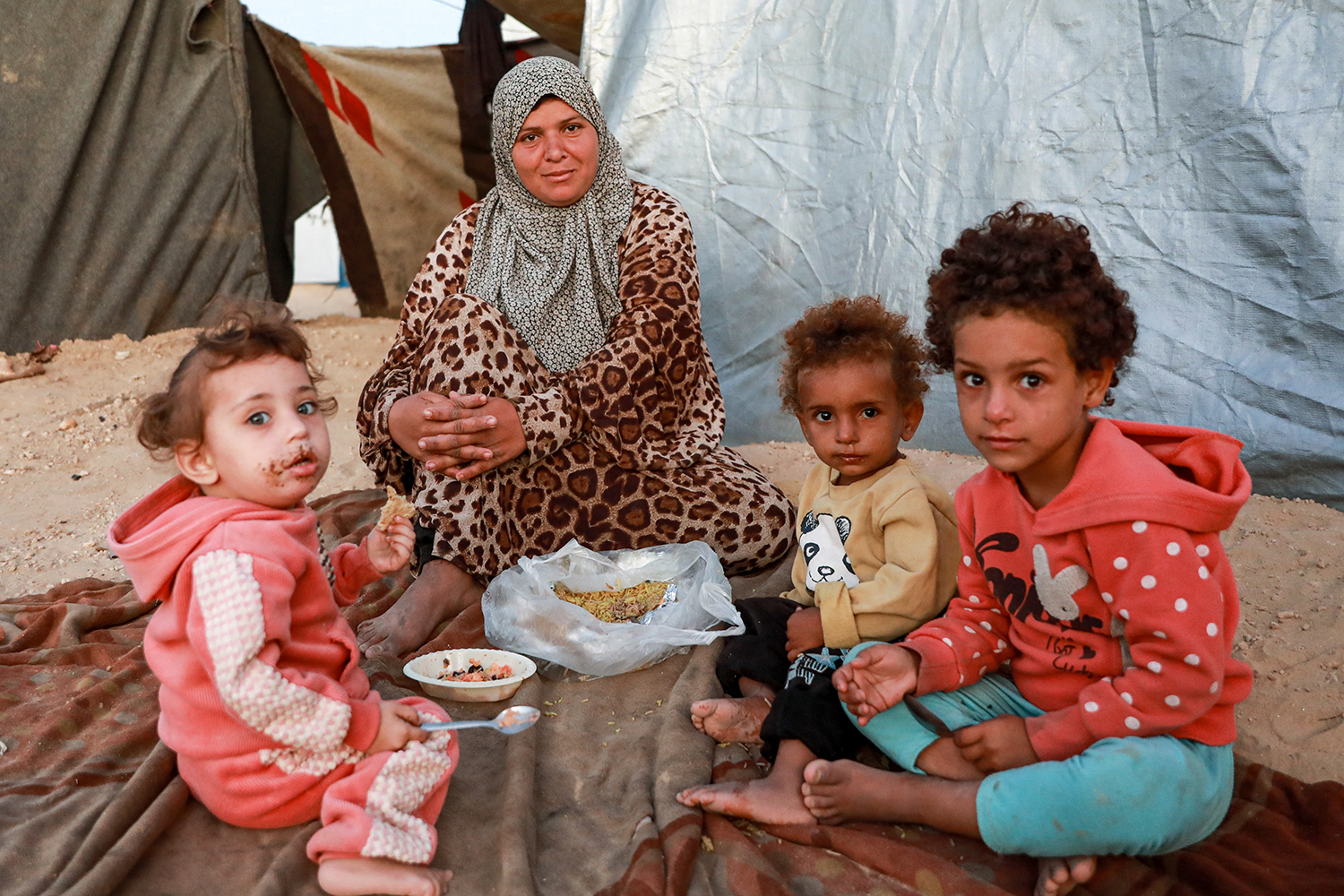Rahma Al Sakani feeding her daughters in front of her tent in Deir al-Balah, Gaza, as Israel's war on civilians there continues