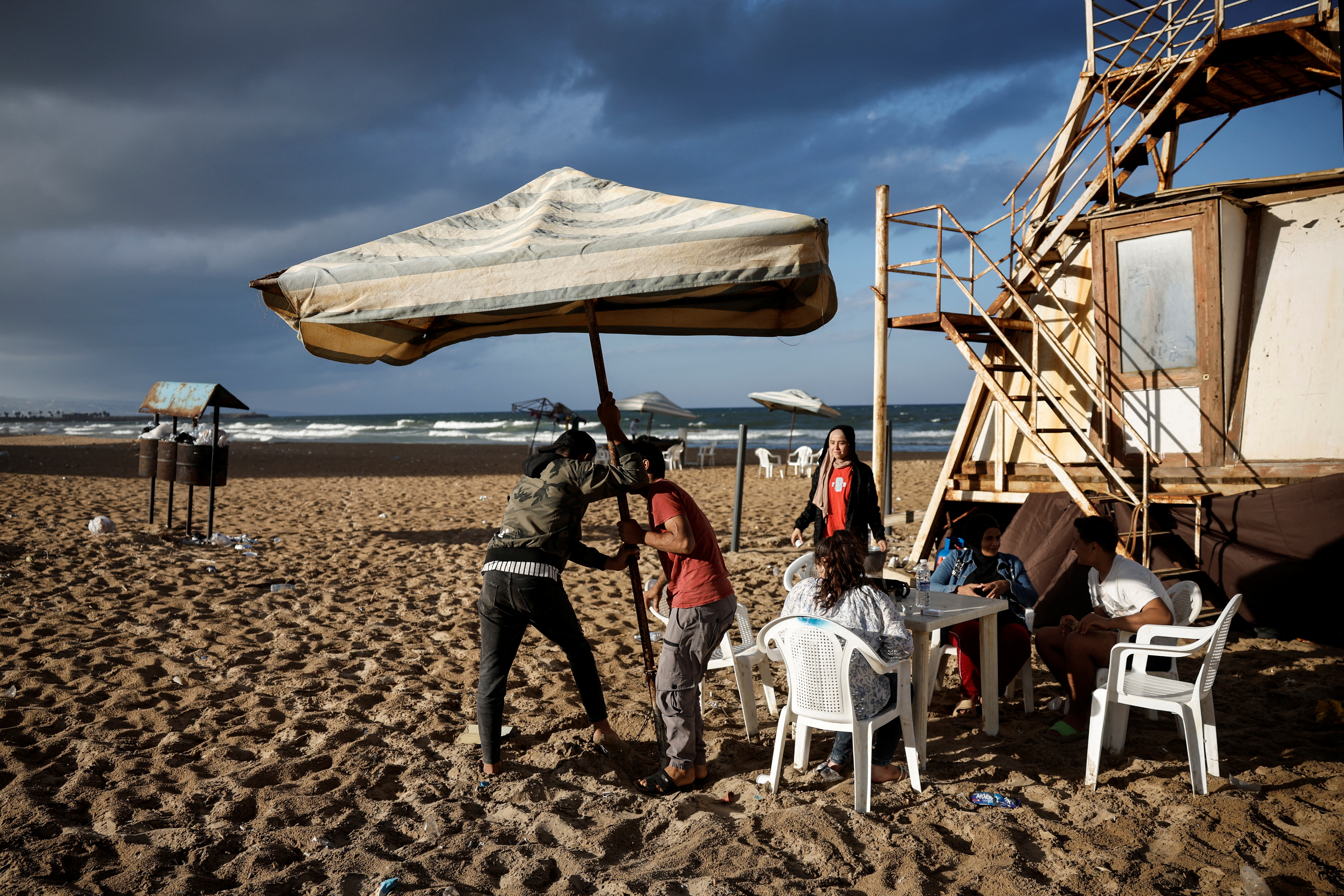 Displaced Syrian man Mohamed Terkmene puts up a parasol for protection against rain at a makeshift encampment where scores of displaced people live, amid hostilities between Hezbollah and Israeli forces, at a beach in Beirut, Lebanon, October 1