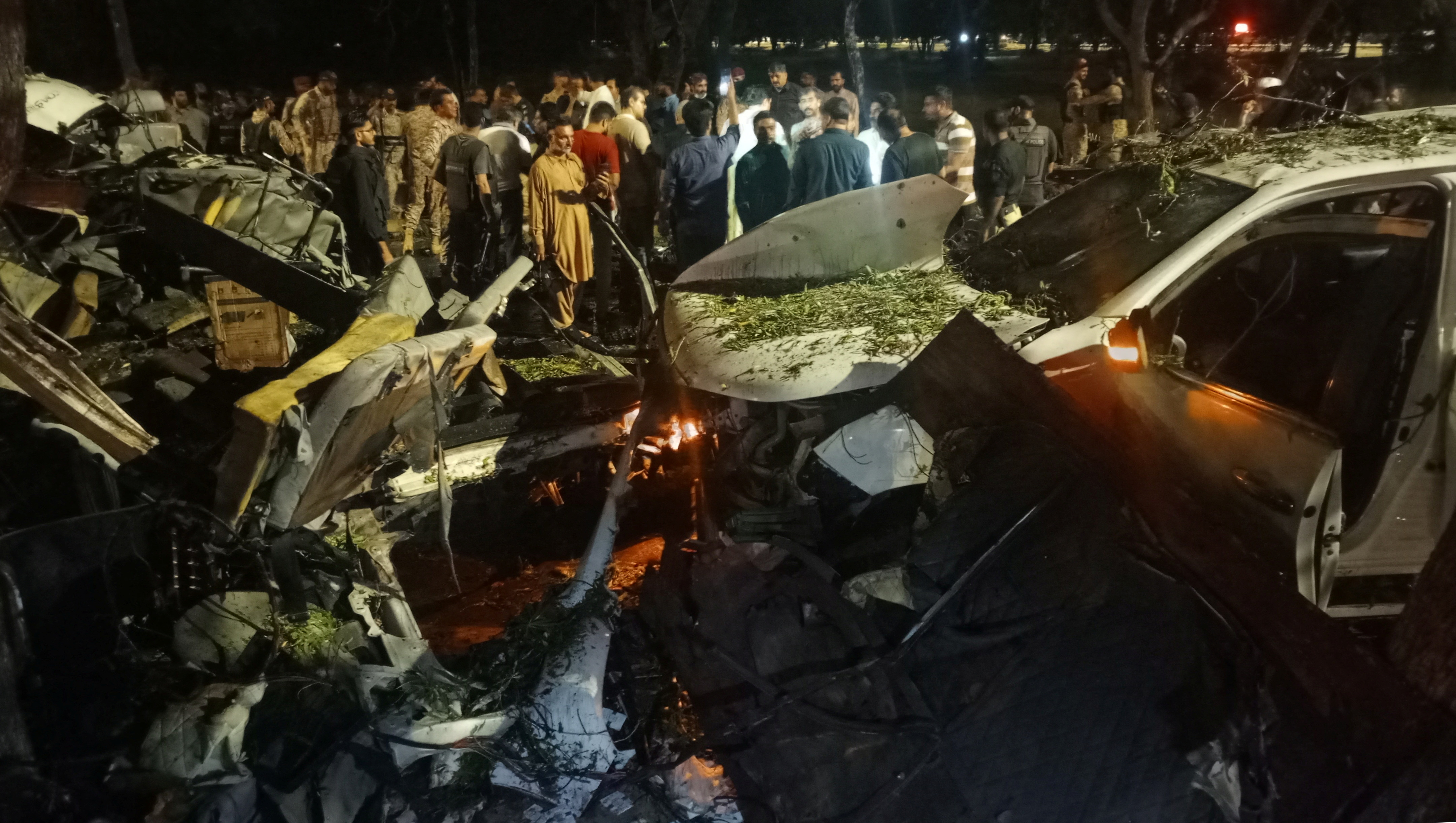 People stand near the wreckage of vehicles as they gather after an explosion near Jinnah International Airport in Karachi