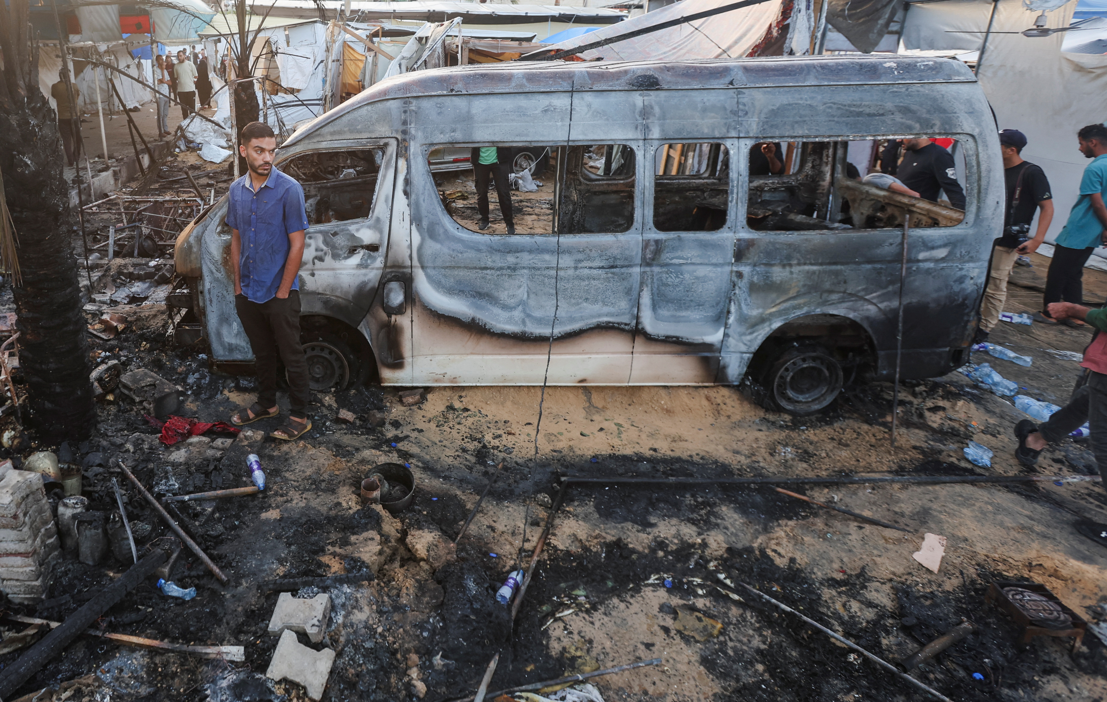 A Palestinian man stands next to a destroyed vehicle at the site of an Israeli strike on tents sheltering displaced people