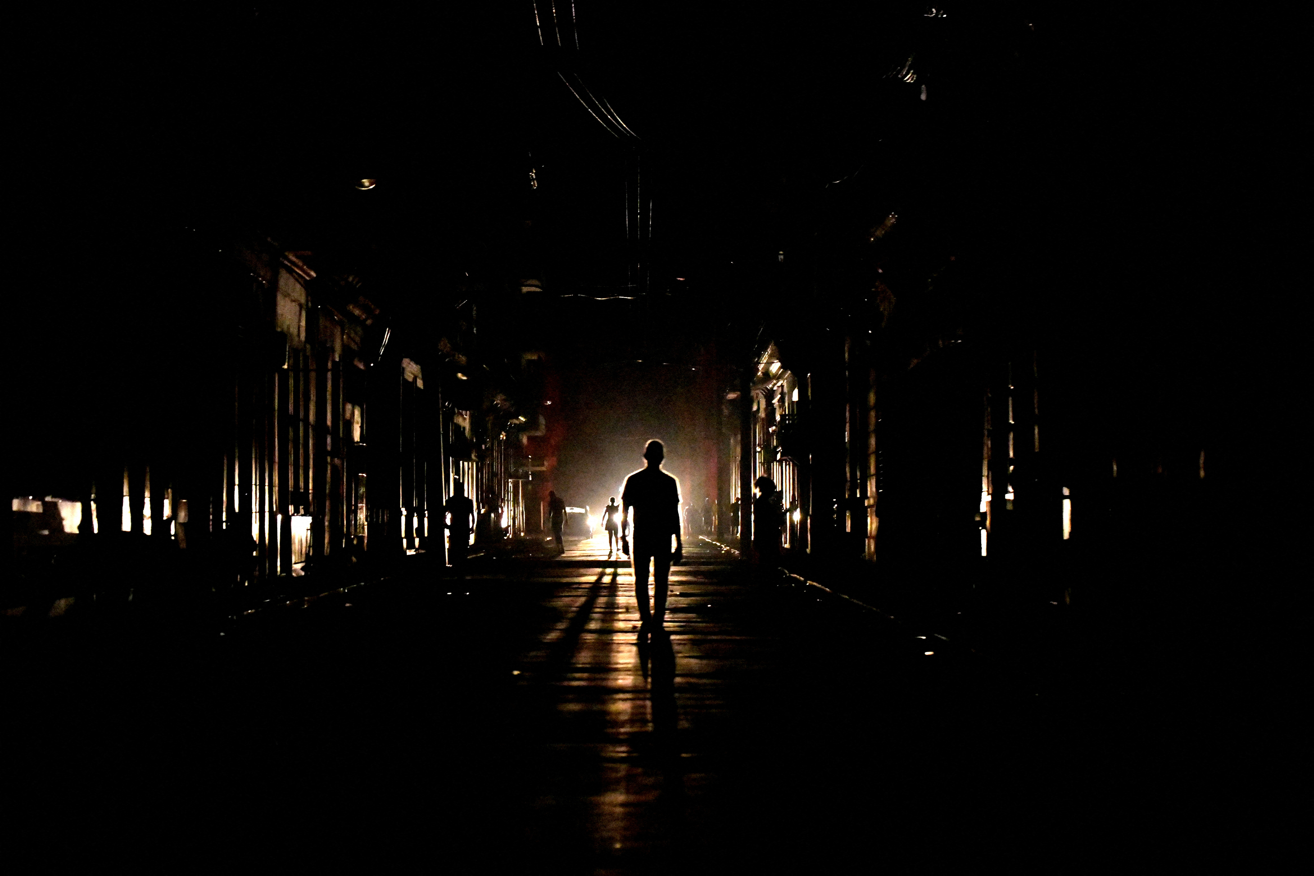 The silhouette of a person is seen against car lights as they walk down a darkened street during a blackout in Havana