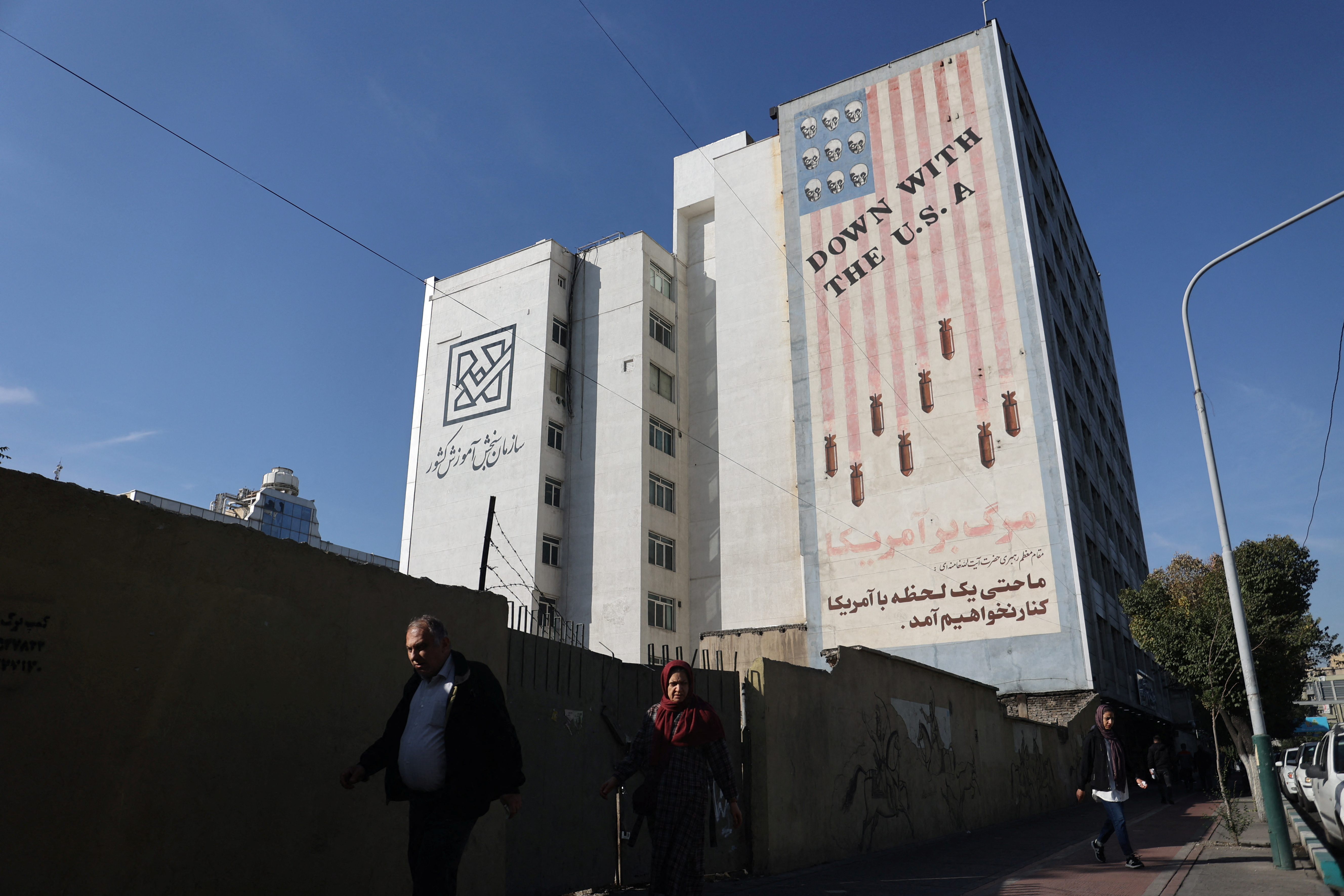 People walk near an anti-U.S. mural on a building after several explosions were heard, in Tehran, Iran, October 26, 2024. 