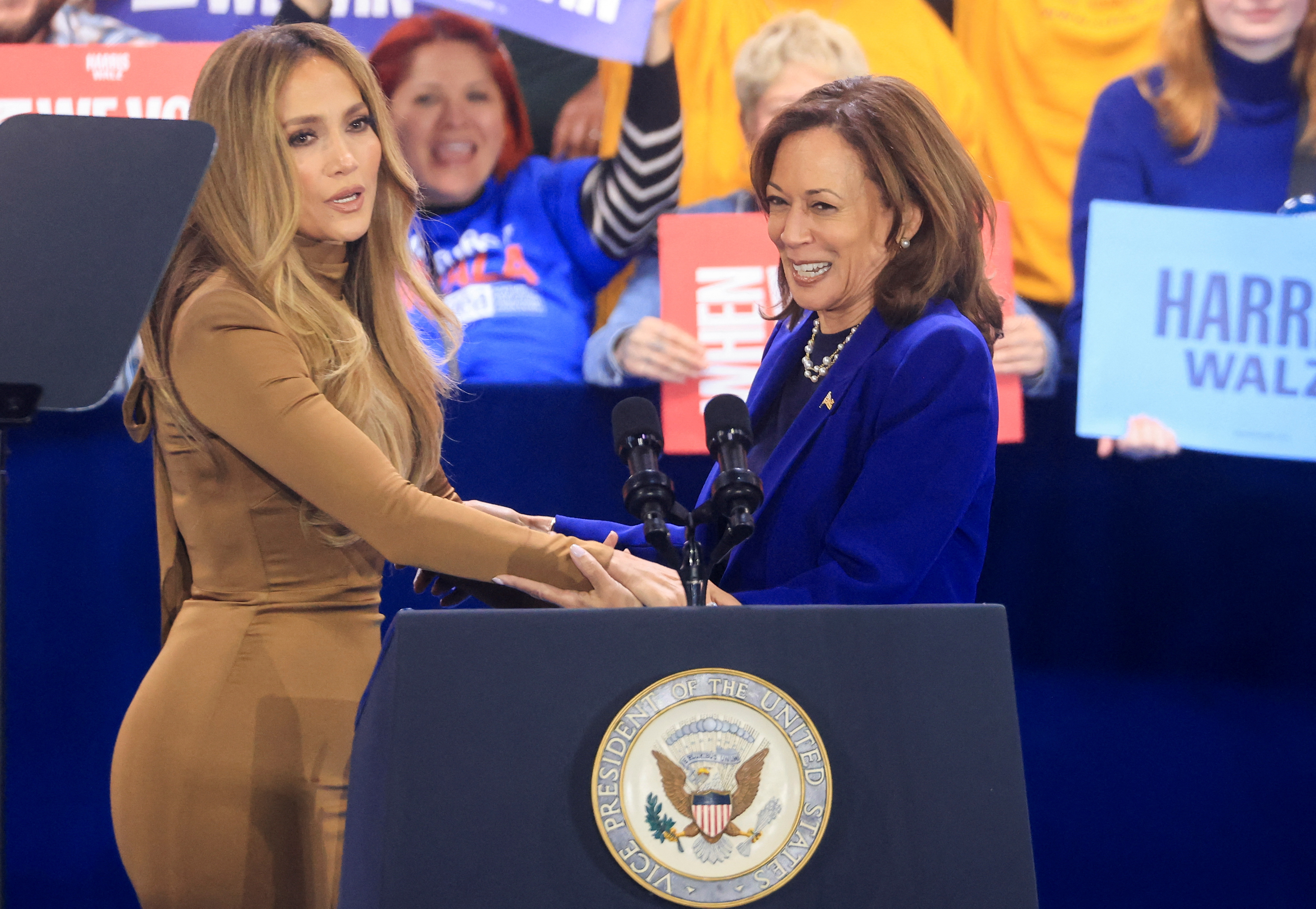 Jennifer Lopez holds hands with Kamala Harris behind a campaign podium in Las Vegas.