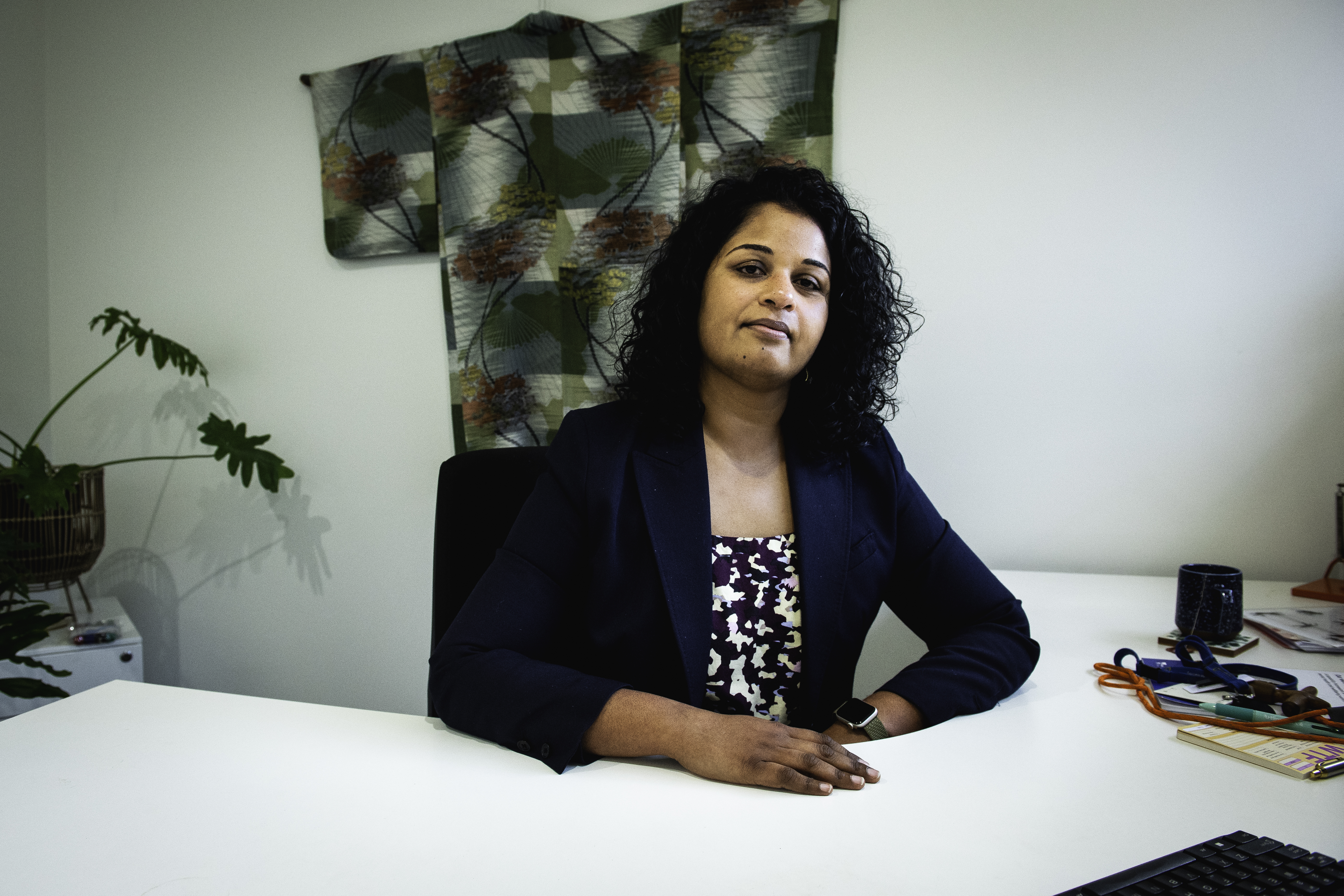 Shalini Arunogiri. She has long dark hair and is wearing a patterned top and black jacket. She's seated behind a desk