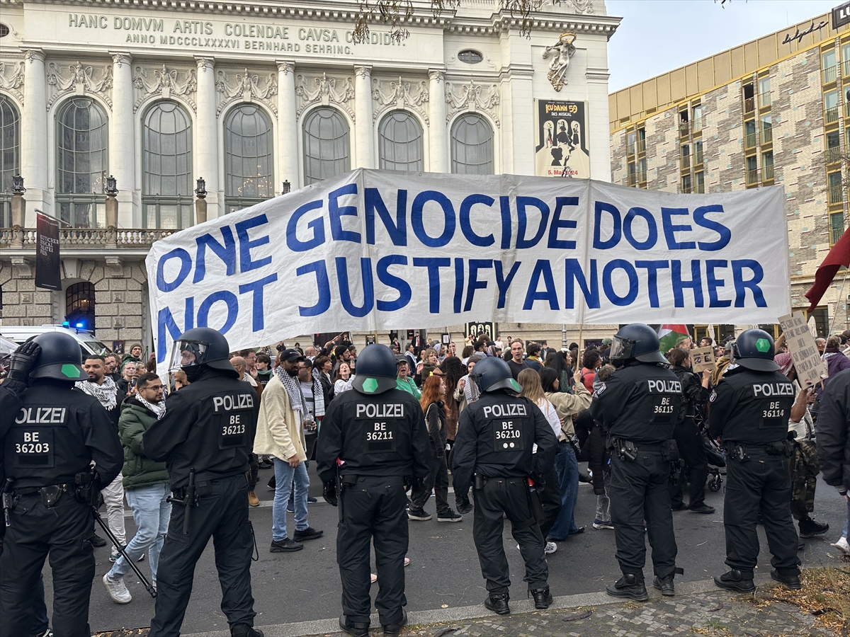 police in dark uniforms surround protestors with a banner saying one genocide does not justify another
