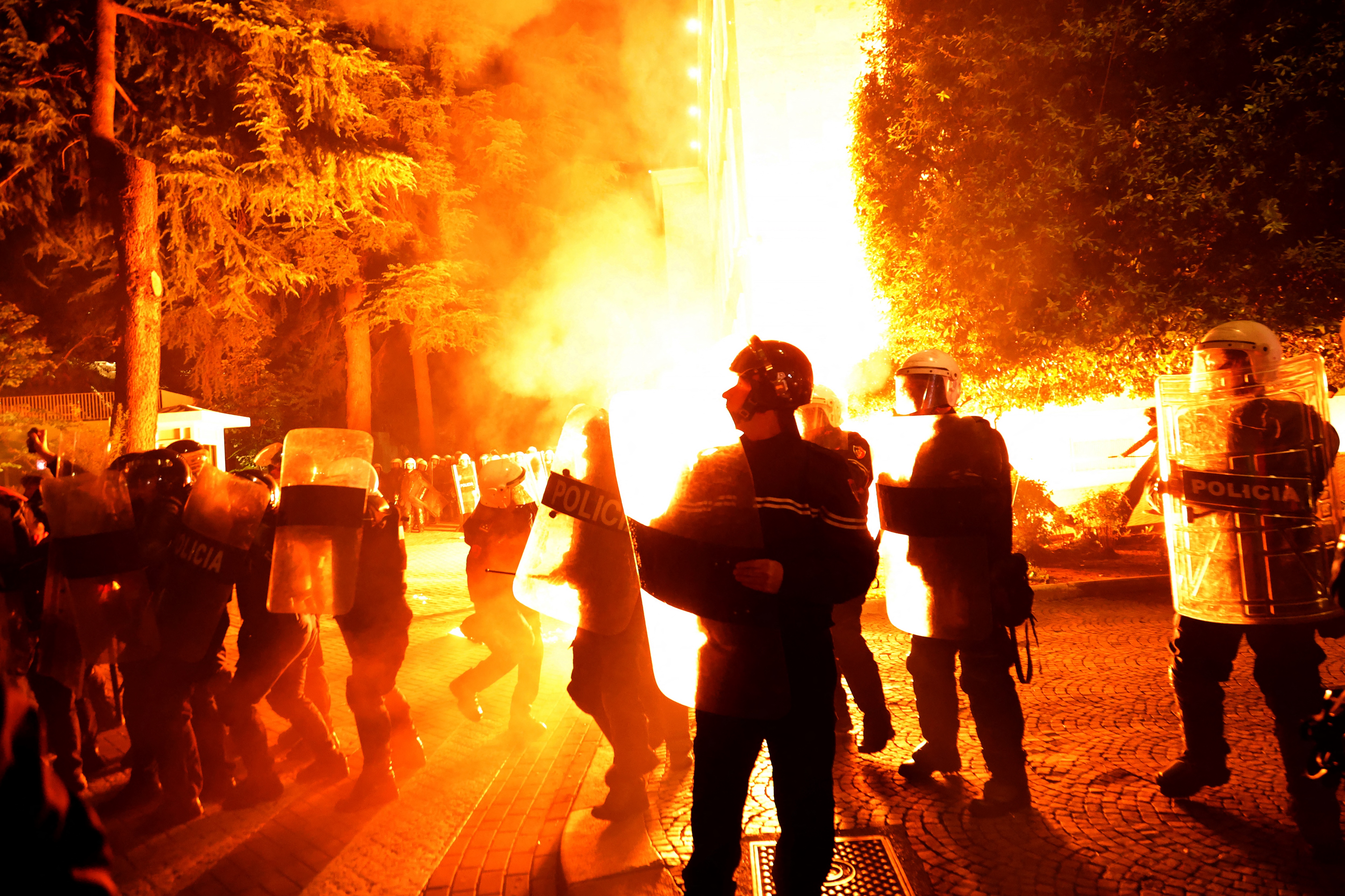 Riot police officers stand in a street as molotov cocktails explode outside the government building, thrown by opposition protesters who demand the resignation of the government and the release of opposition MP Ervin Salianji, in Tirana, on October 7, 2024. - Clashes broke out late Monday in Tirana between police and opposition protesters seeking that longtime leftist Prime Minister Edi Rama resigns, leaving 10 officers injured police said. A few thousand people gathered in the Albanian capital at demonstrations organised by the country's right-wing opposition, according to an AFP reporter. (Photo by Adnan Beci / AFP)