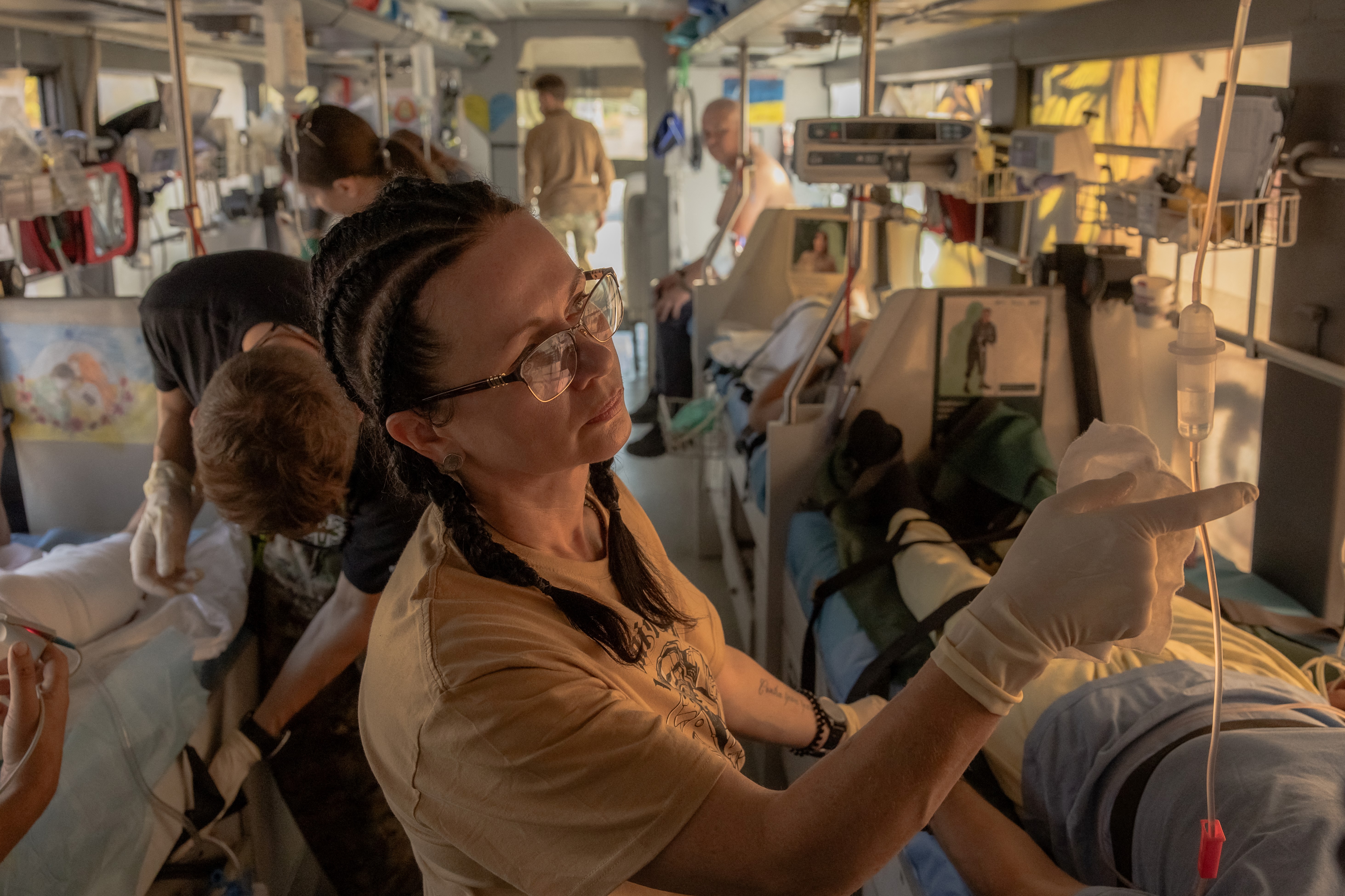 a volunteer medic checking an injured Ukrainian soldier being evacuated on a special bus. Otehr soldlers are on beds along the sides of the bus with volunteer medics on the central aisle.