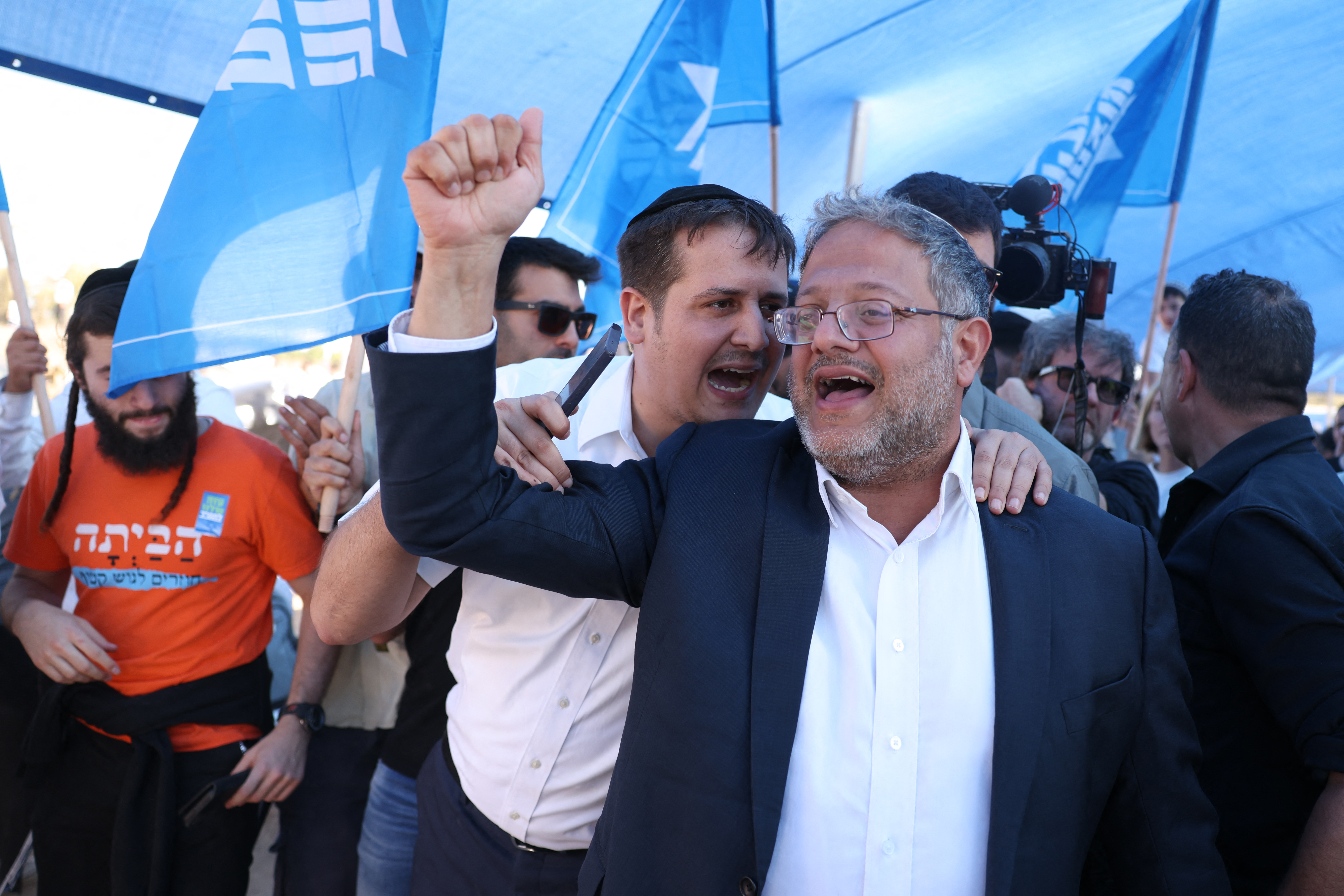 a man in a shirt and jacket raises his fist as another man speaks in his ear
