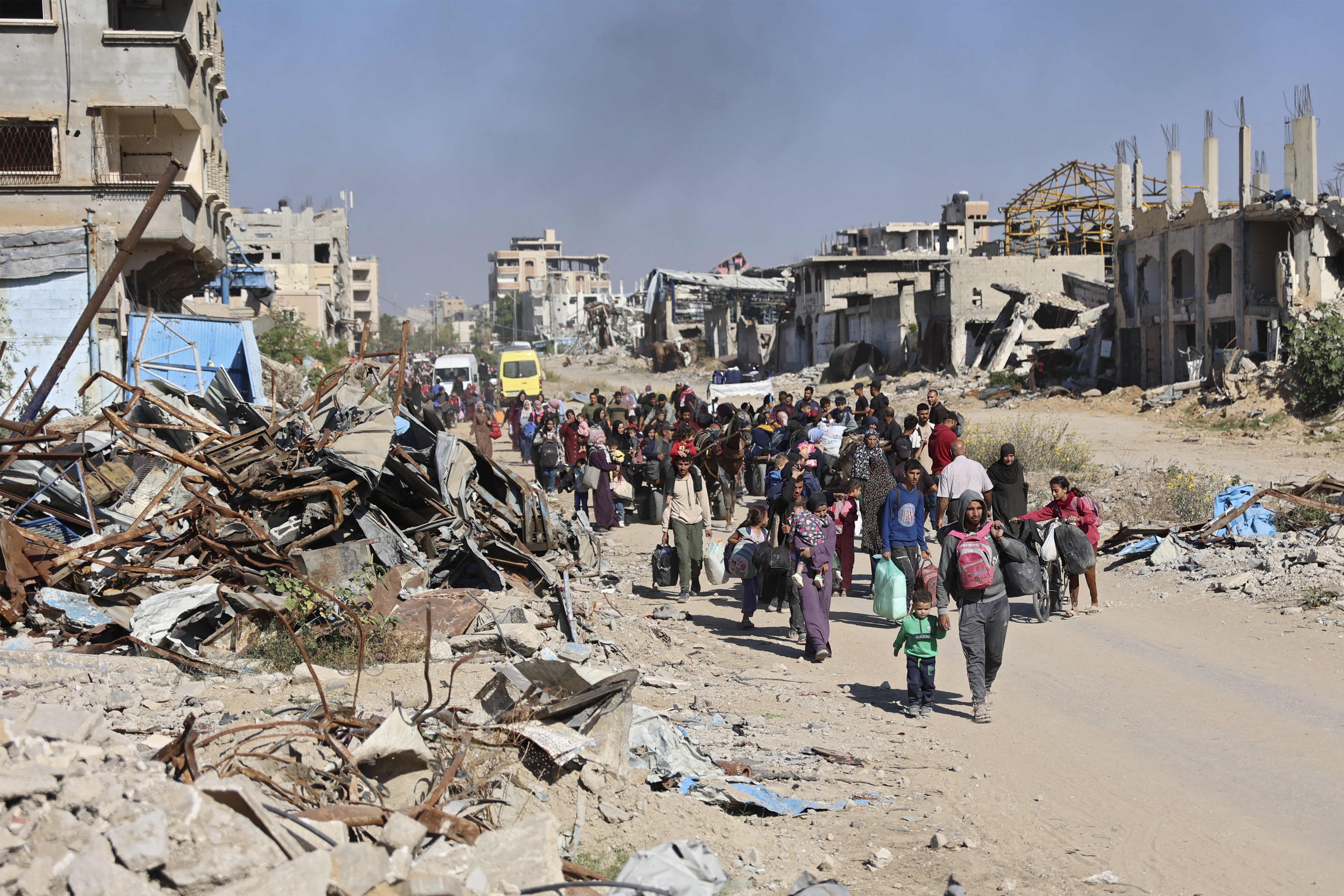 People walk past destroyed buildings carrying their belongings