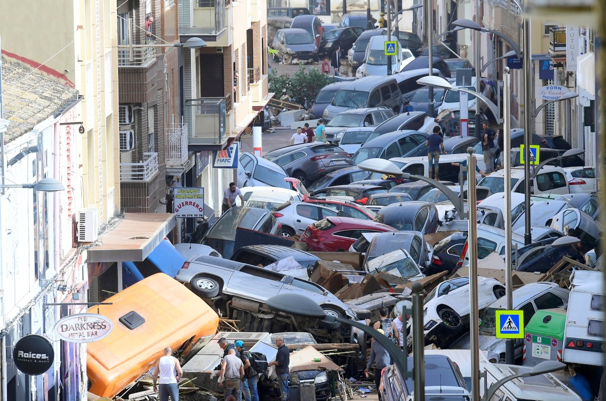 Pedestrians stand next to piled-up cars following deadly floods