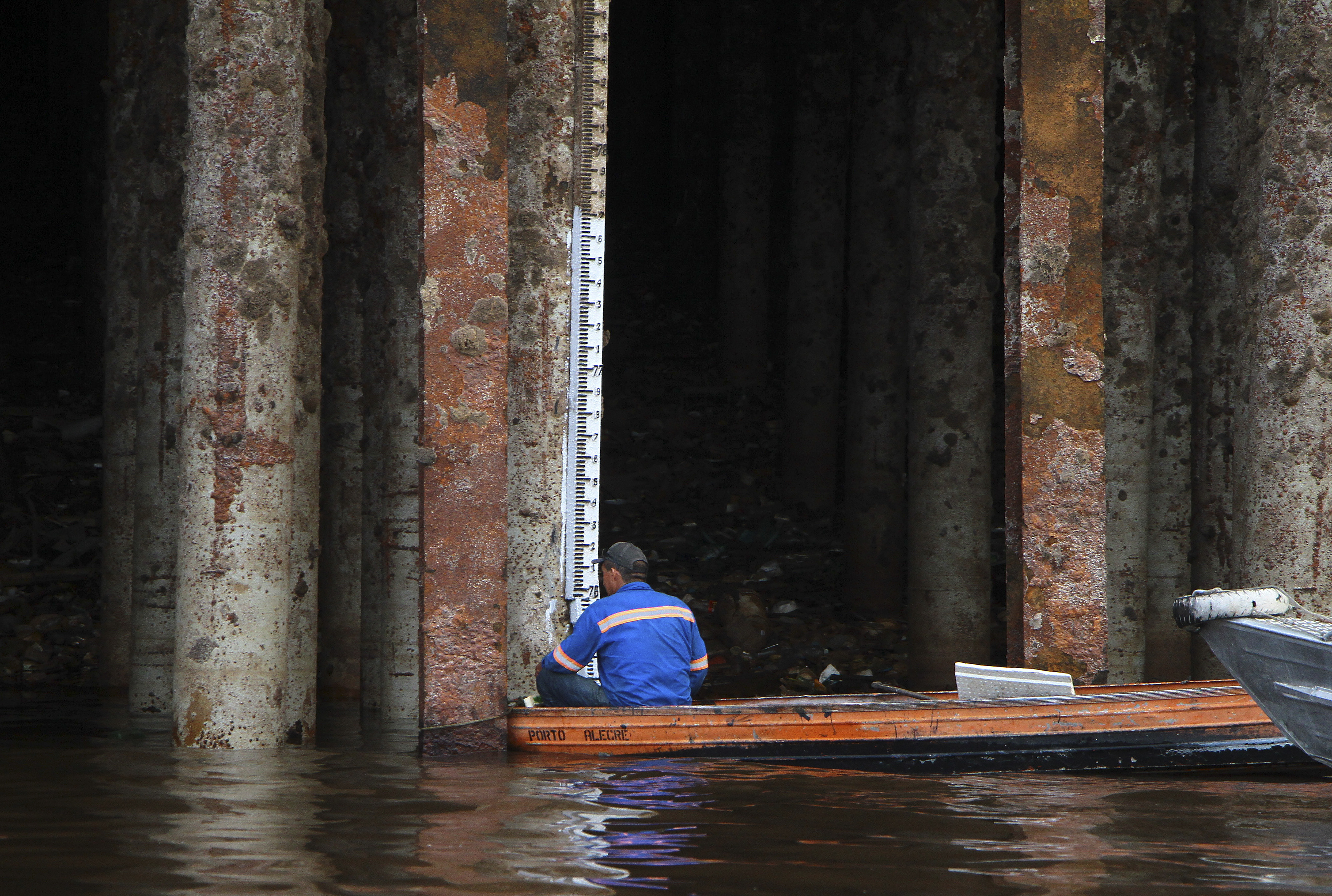 A dock worker measures the water levels on the Rio Negro, using a small boat to look at a measuring stick affixed to the dock.