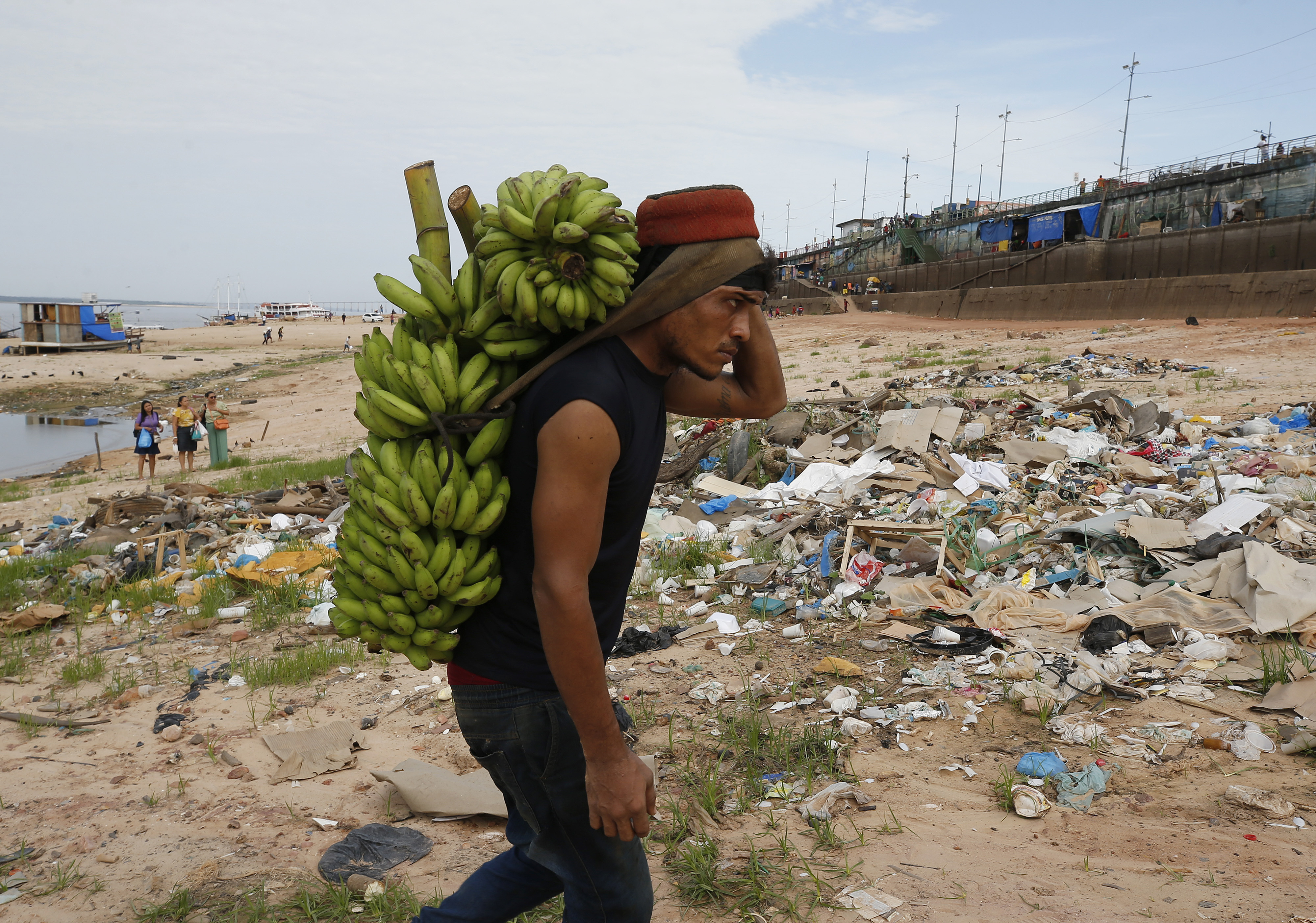 A man carries a branch of bananas across a dry riverbank.