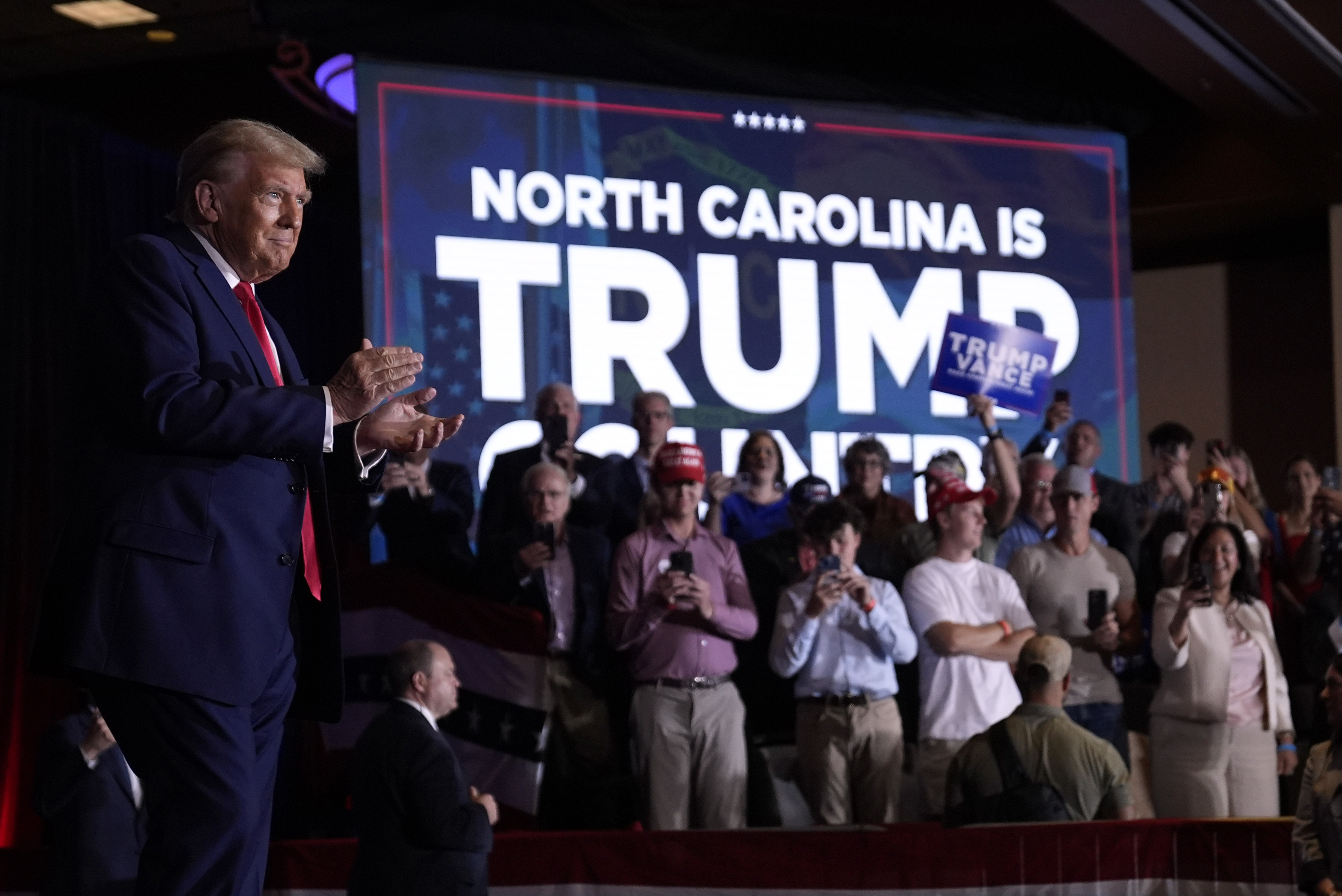 Donald Trump rallies in front of a sign that reads,