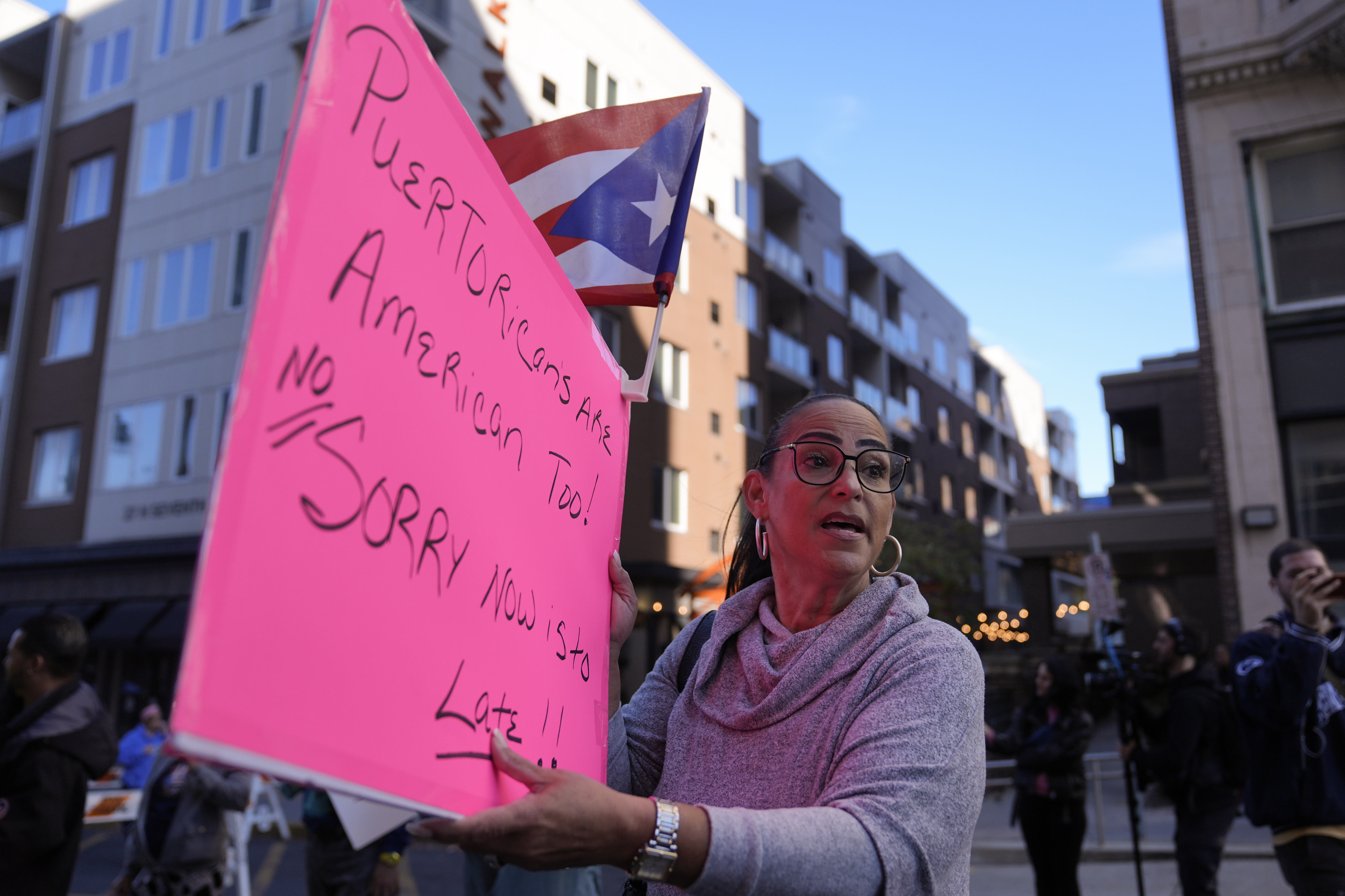 A protester holds a pink poster board with a handwritten sign.