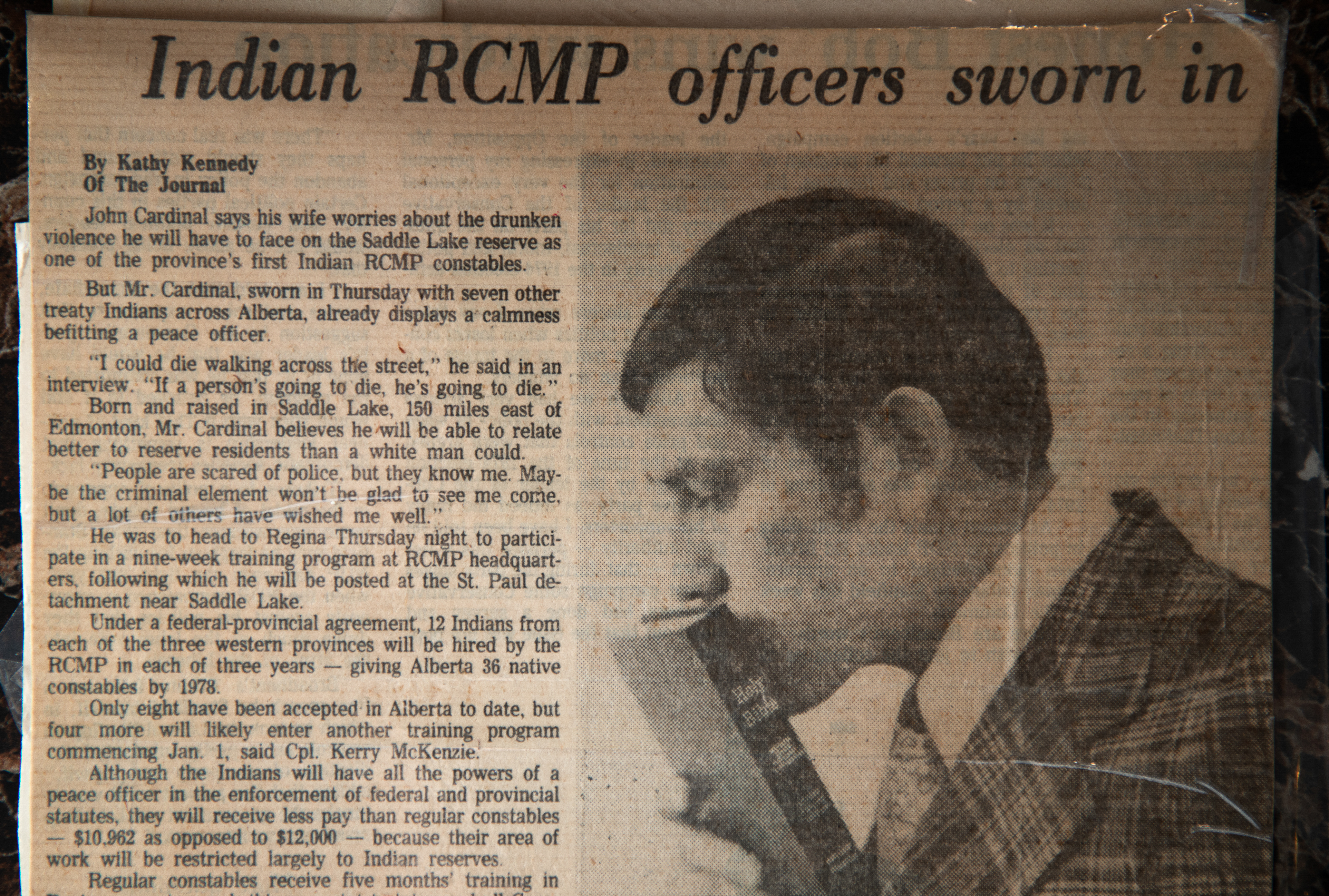 A newspaper cutting shows a man kissing a Bible. The headline says 'Indian RCMP officers sworn in'