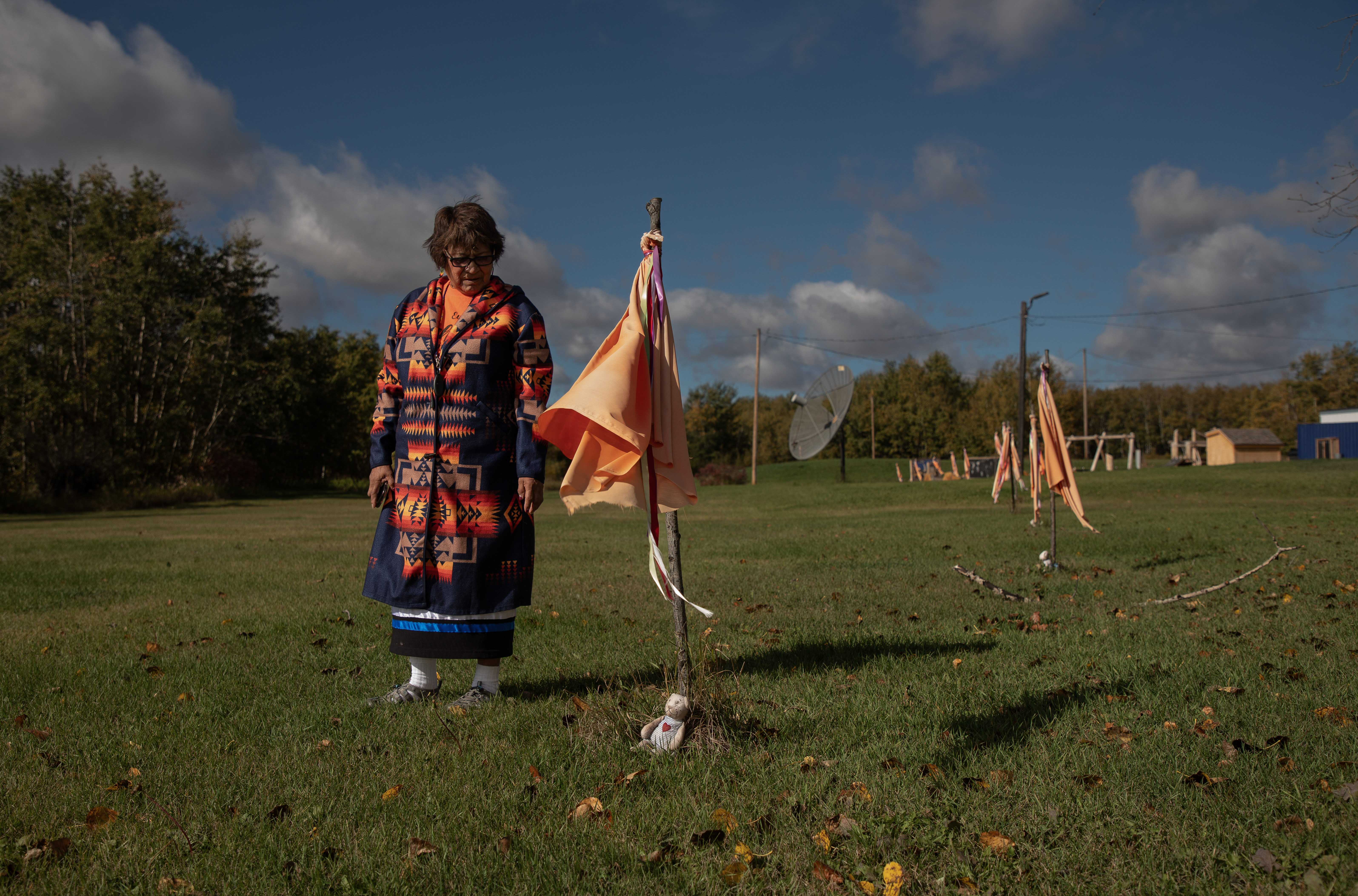 A woman stands by makeshift flags that have been planted in a green field