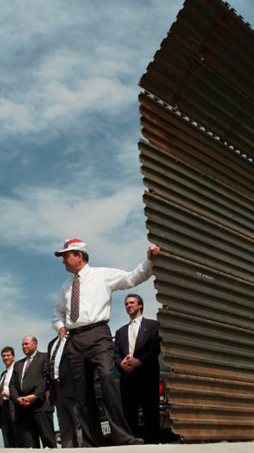 Pat Buchanan poses, leaning against the US-Mexico border wall in the 1990s.