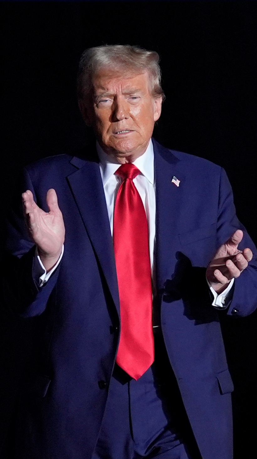 Donald Trump claps at a rally, as he walks past a row of US flags under a "Make America Great Again" sign.