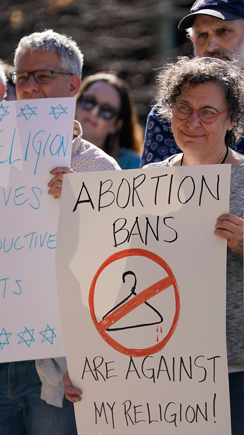 Protesters hold up hand-written signs warning about the dangers of abortion bans, including one that reads: "Abortion bans are against my religion," with a clothes hanger crossed out.