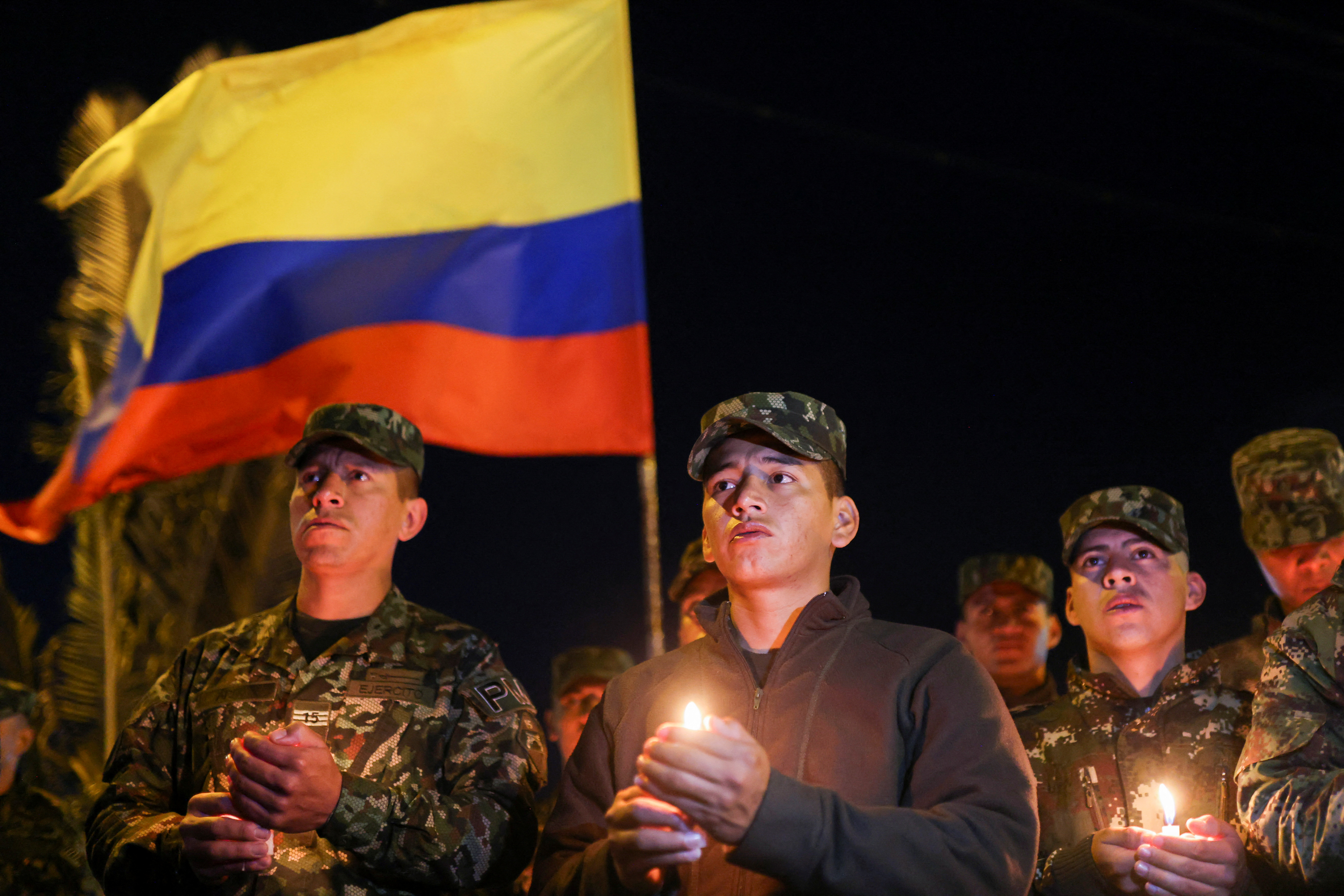 A Colombian soldier, dressed in fatigues, holds a candle and a Colombian flag at a vigil