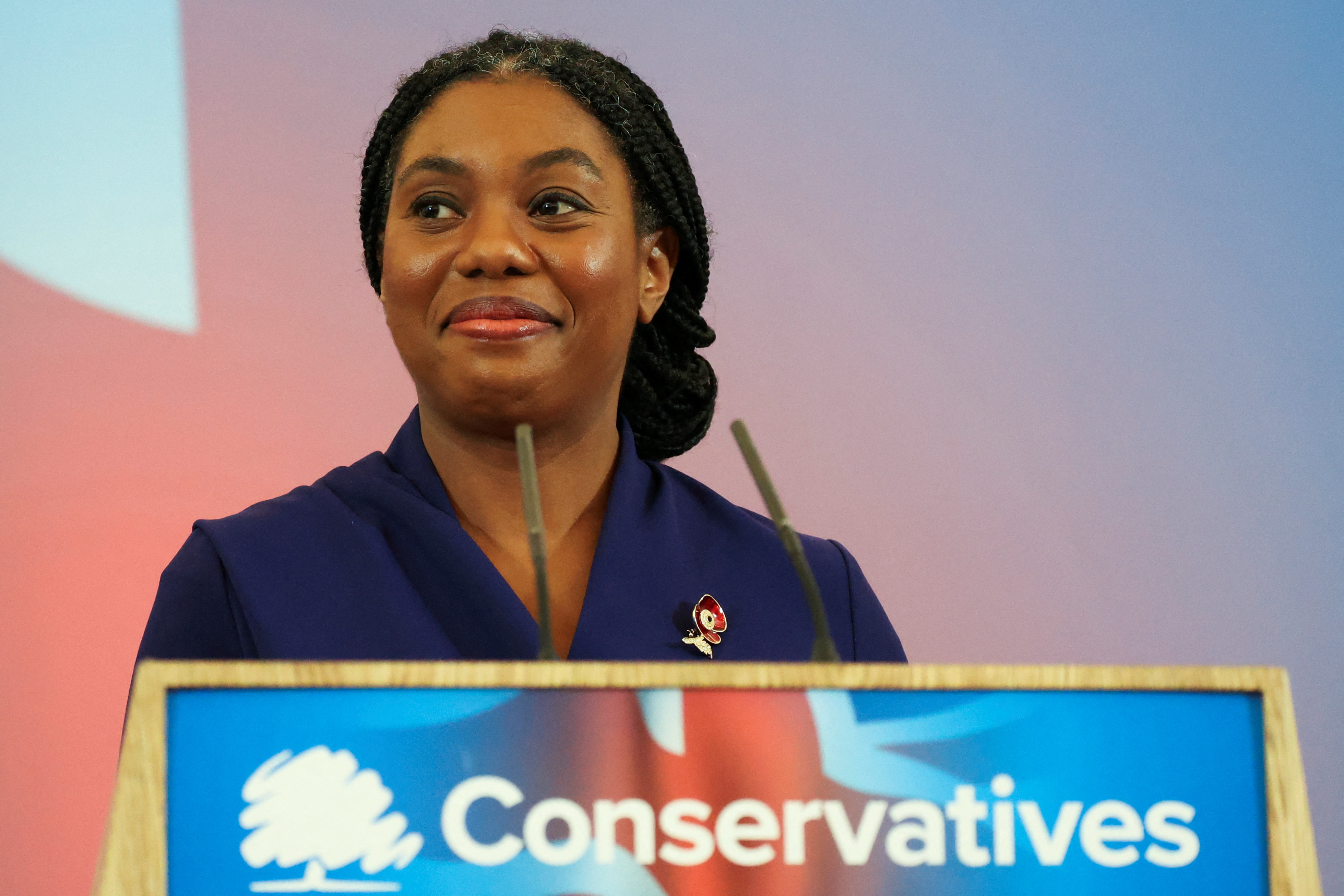 Kemi Badenoch smiles as she stands at a podium with the Conservative Party logo on it