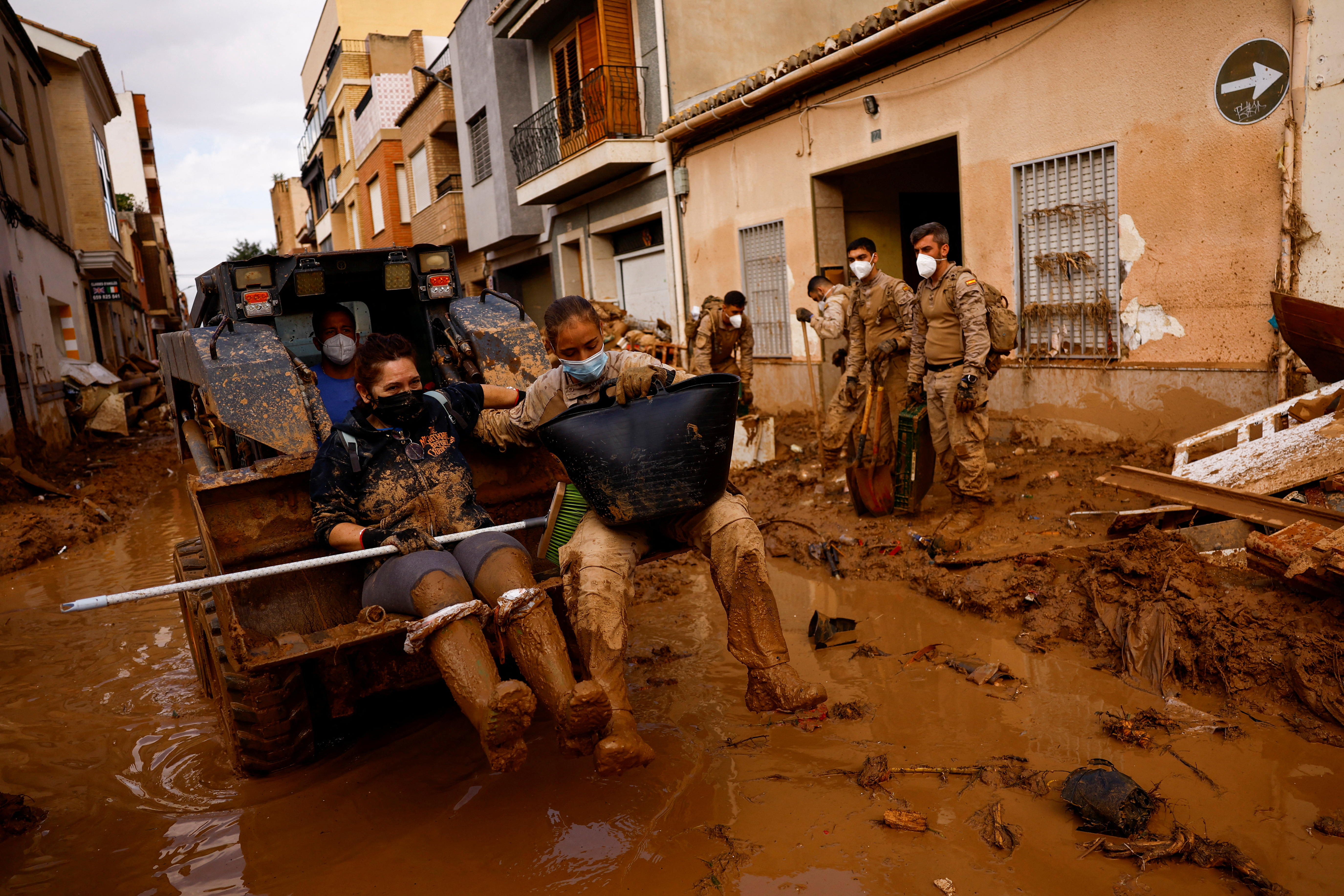 Susana Costa and a member of the Spanish military are transported with an excavator on a street covered in mud in Massanassa, Spain