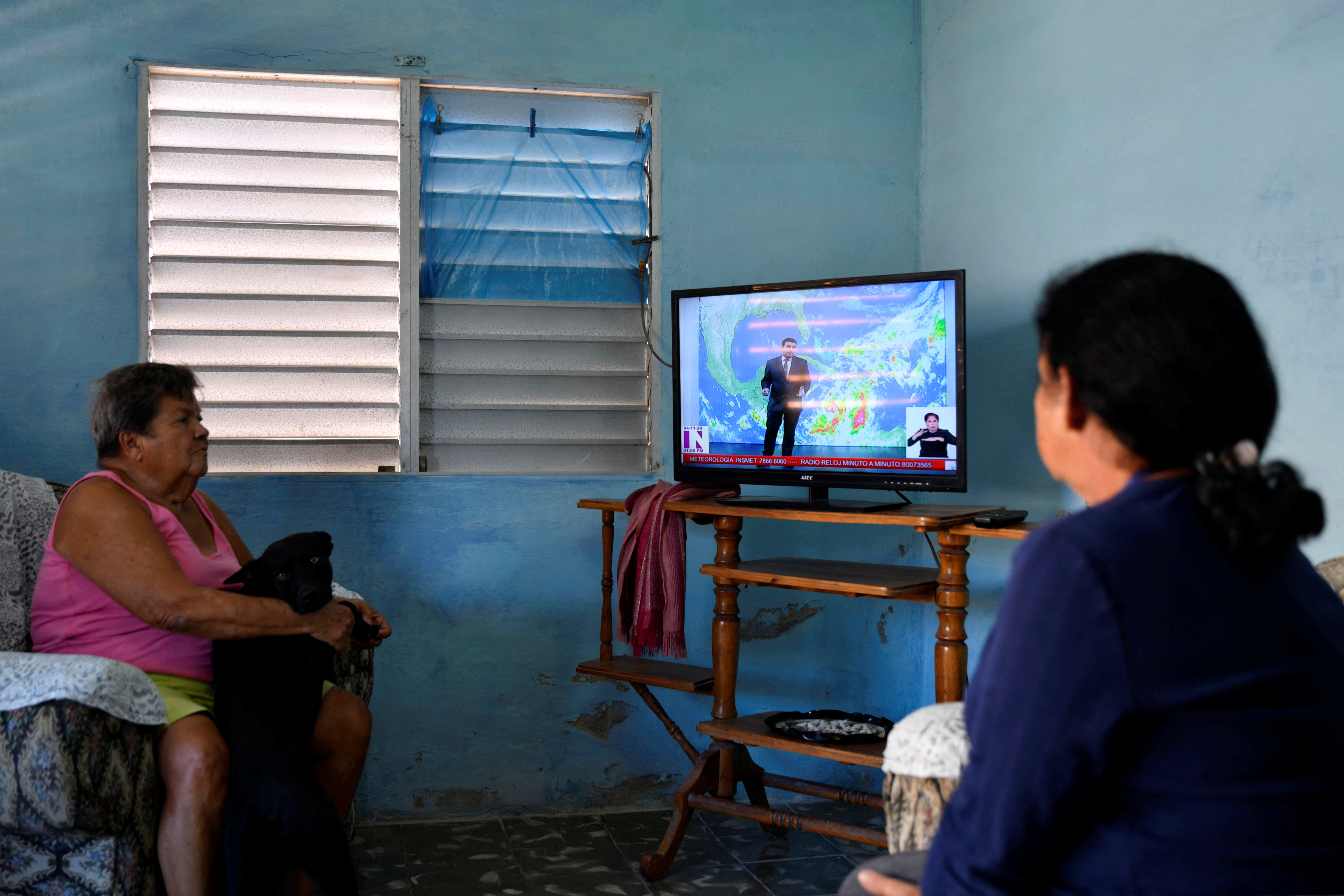 A woman and her daughter watch TV coverage of Tropical Storm Rafael in Cuba