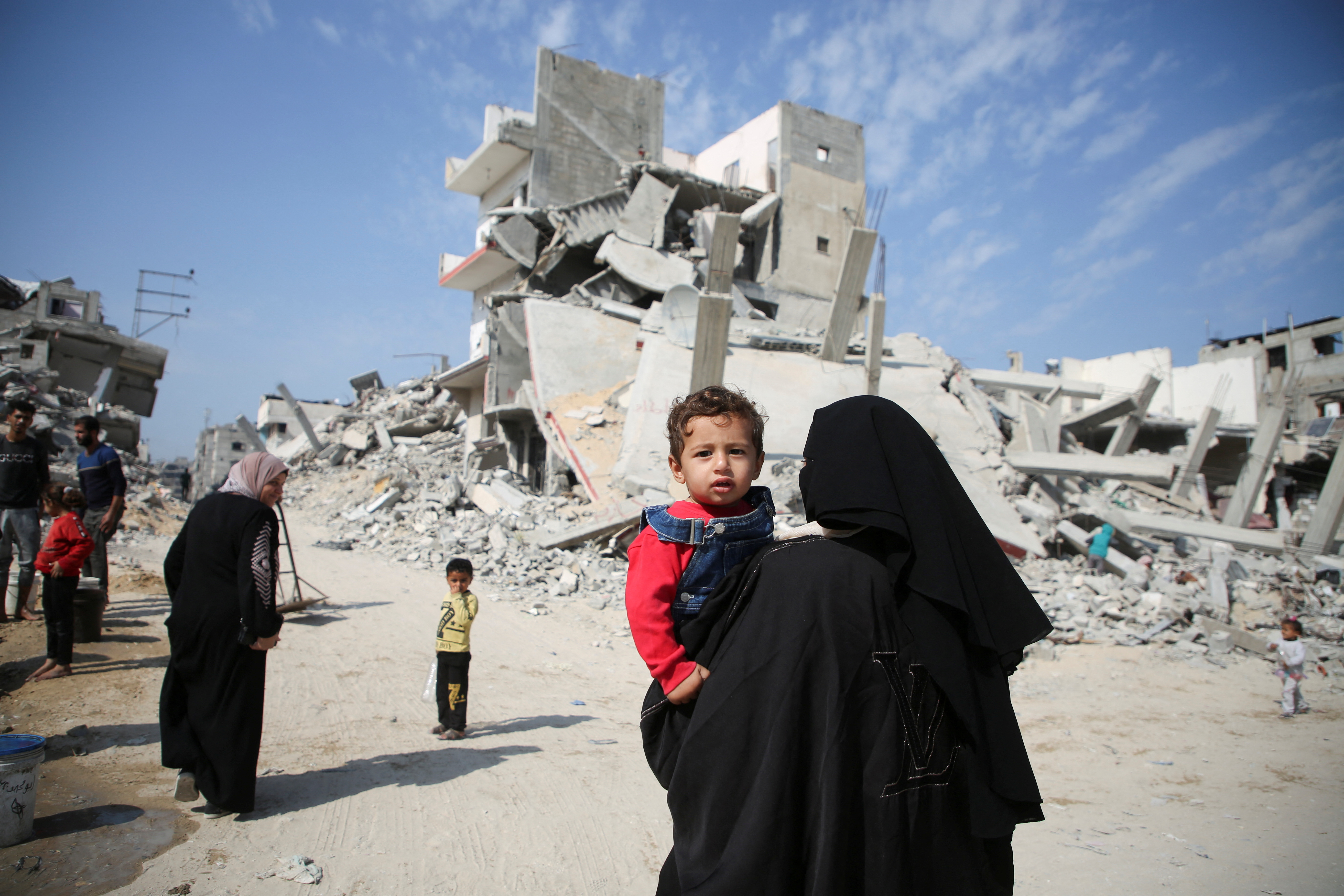 A Palestinian woman carries a child as they walk past the rubble of houses destroyed in previous strikes during the Israeli military offensive, amid the Israel-Hamas conflict, in Khan Younis in the southern Gaza Strip November 6, 2024. REUTERS/Hatem Khaled TPX IMAGES OF THE DAY