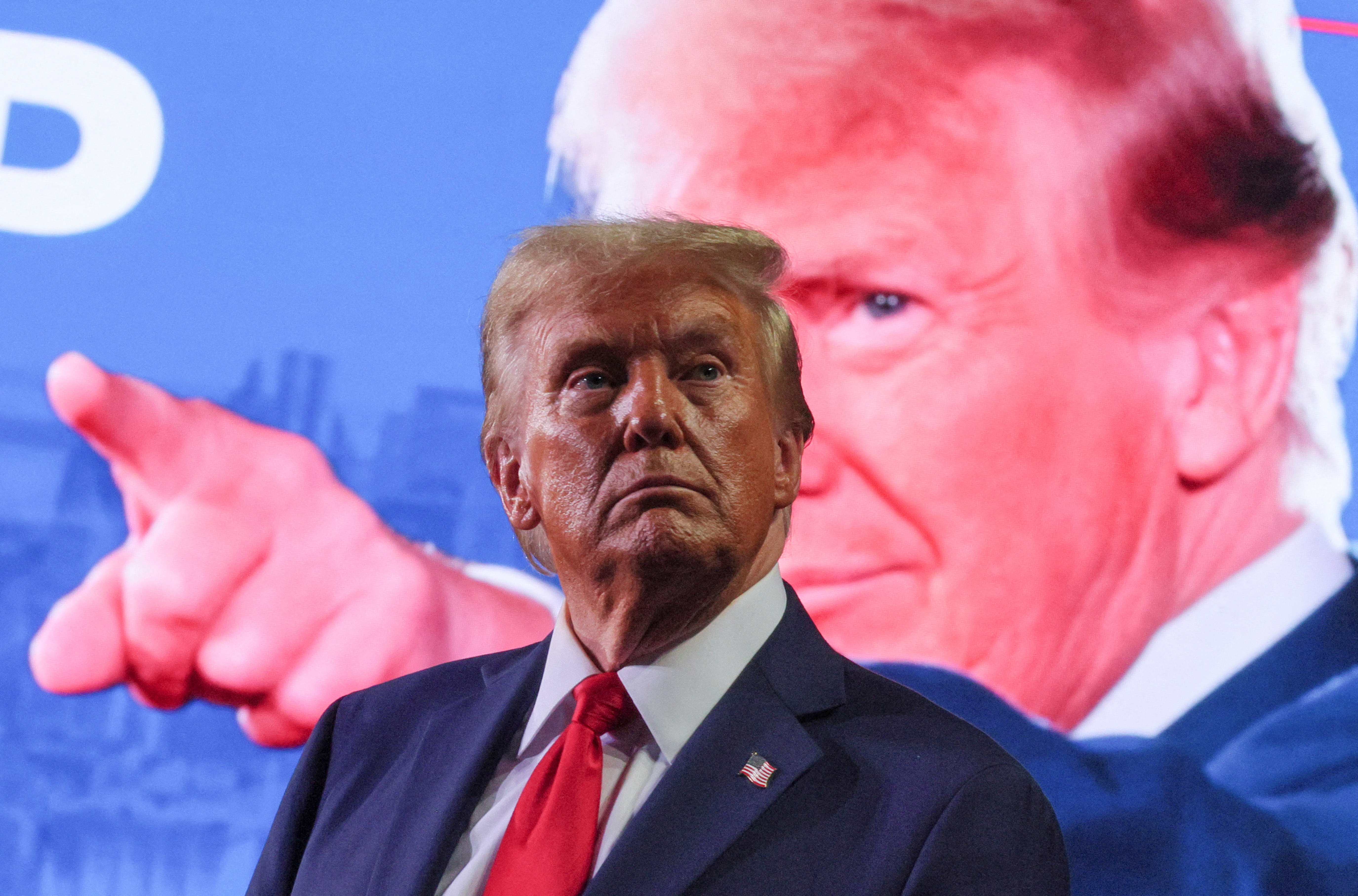 Donald Trump stands in front of a billboard of himself