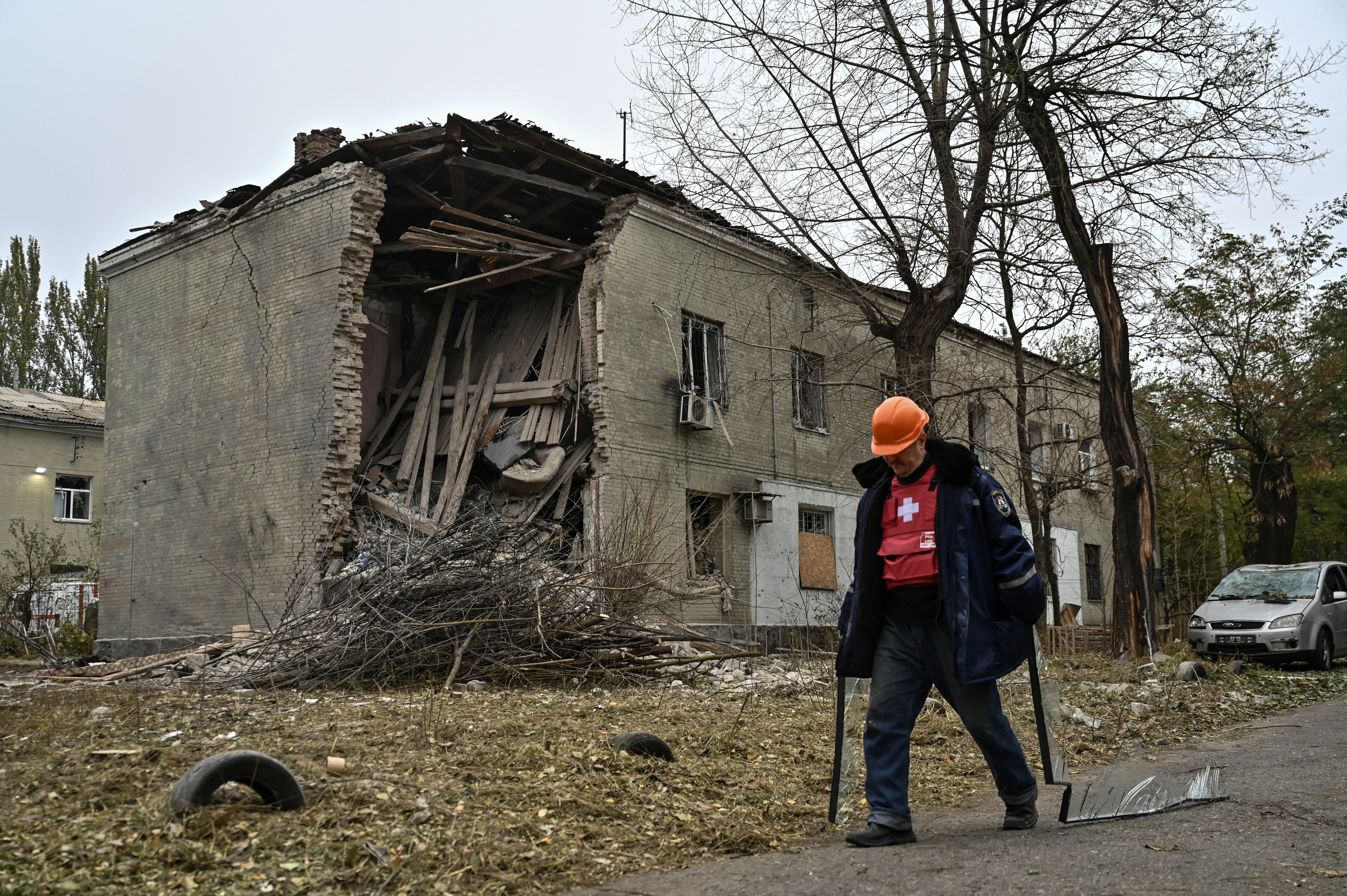 A municipal worker carries broken glass as he walks past an apartment building hit by a Russian air strike,
