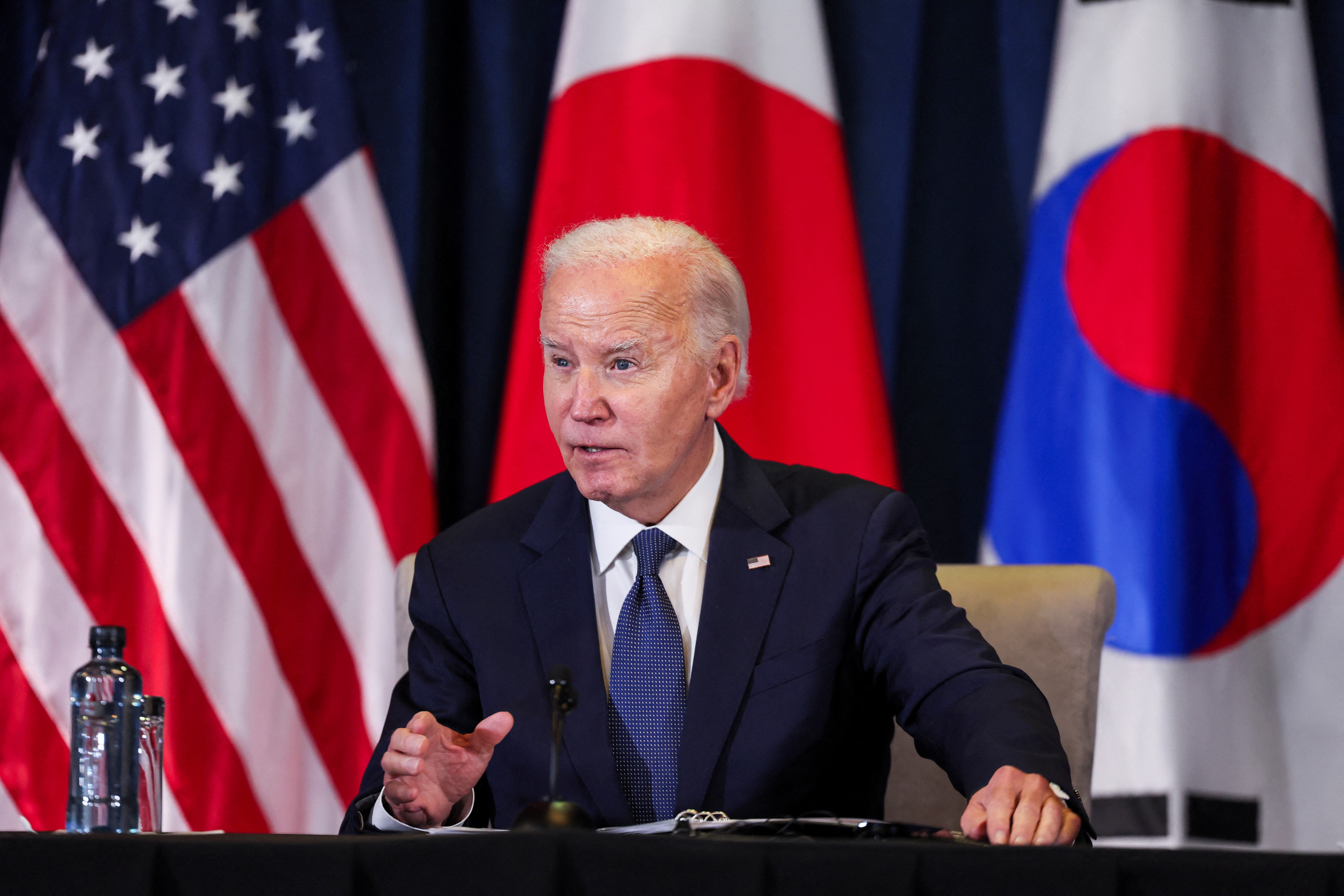 Joe Biden at a press conference, in front of US, South Korean and Japanese flags