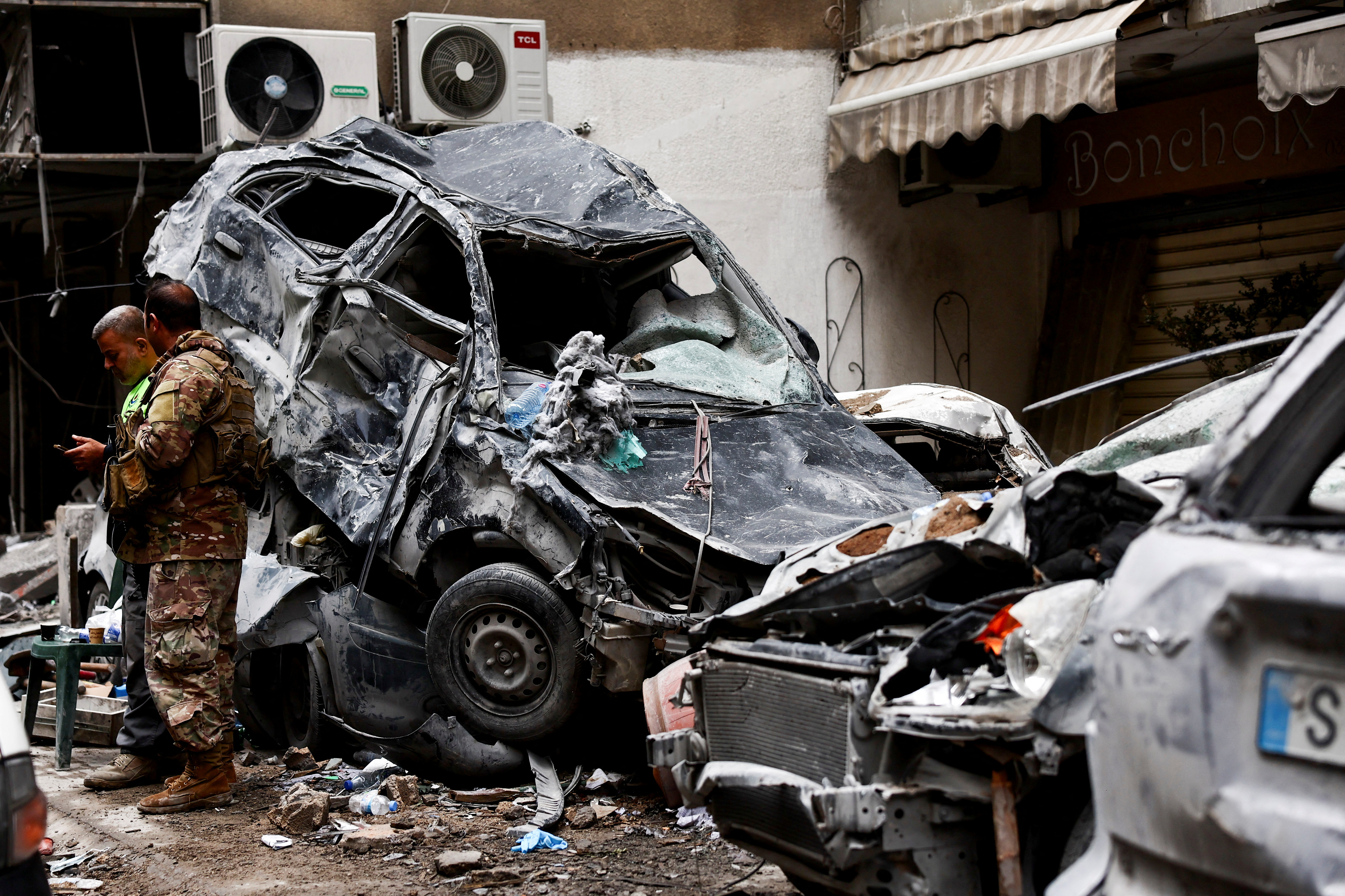 A Lebanese army soldier and a civil defense member stand near damaged cars at a site in the aftermath of Israeli strikes