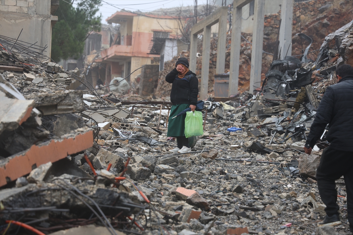 a woman wipes away tears as she stands in between destroyed buildings