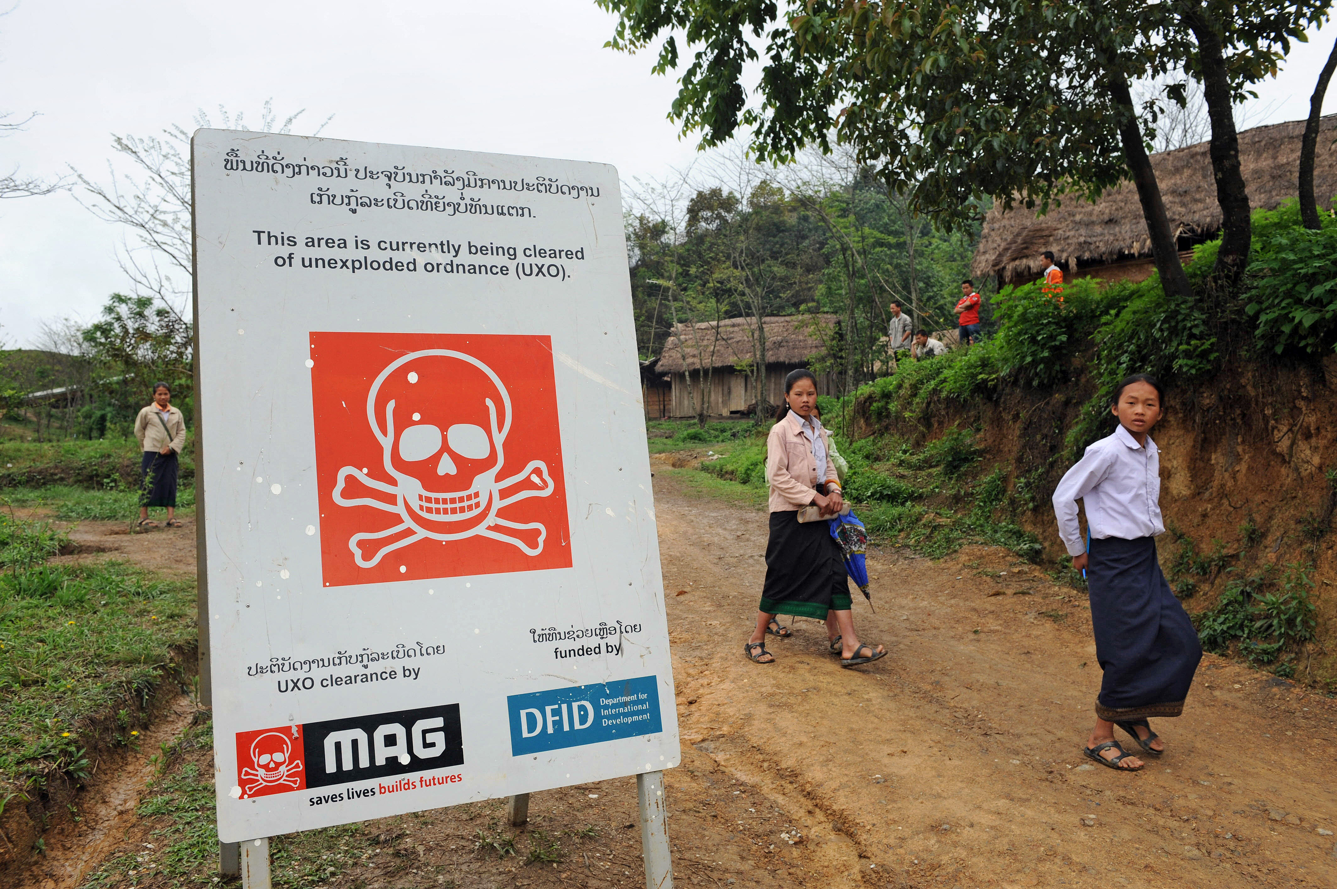 TO GO WITH Laos-US-military-explosives-clearance,FEATURE by Frank Zeller Students walk past a poster warning the area is under a mine clearance operation by an UXO (unexploded ordnance) clearance team seconded by the British Mines Advisory Group (MAG) at the site of the Phuckae secondary school in the northern province of Xiangkhoang on April 03, 2008. Laos, a sleepy Southeast Asian backwater, during the Vietnam War became the world's most heavily bombed country per head of population, with US bombers flying about 80,000 missions in the 1960s and 70s. AFP PHOTO/HOANG DINH Nam (Photo by HOANG DINH NAM / AFP)