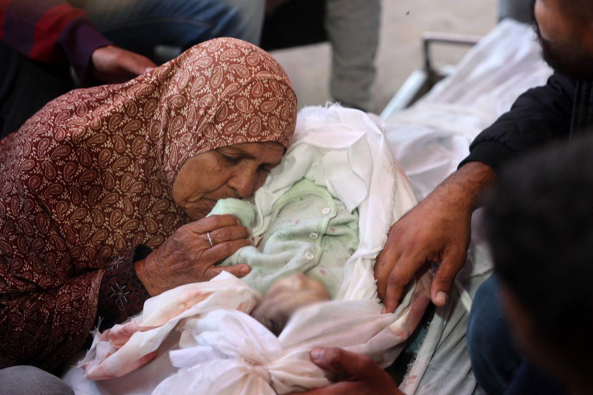 Nakba survivor Majdiya kisses the hand of her great grandson Tamer who was killed by Israeli bombardment in a hospital in central Gaza
