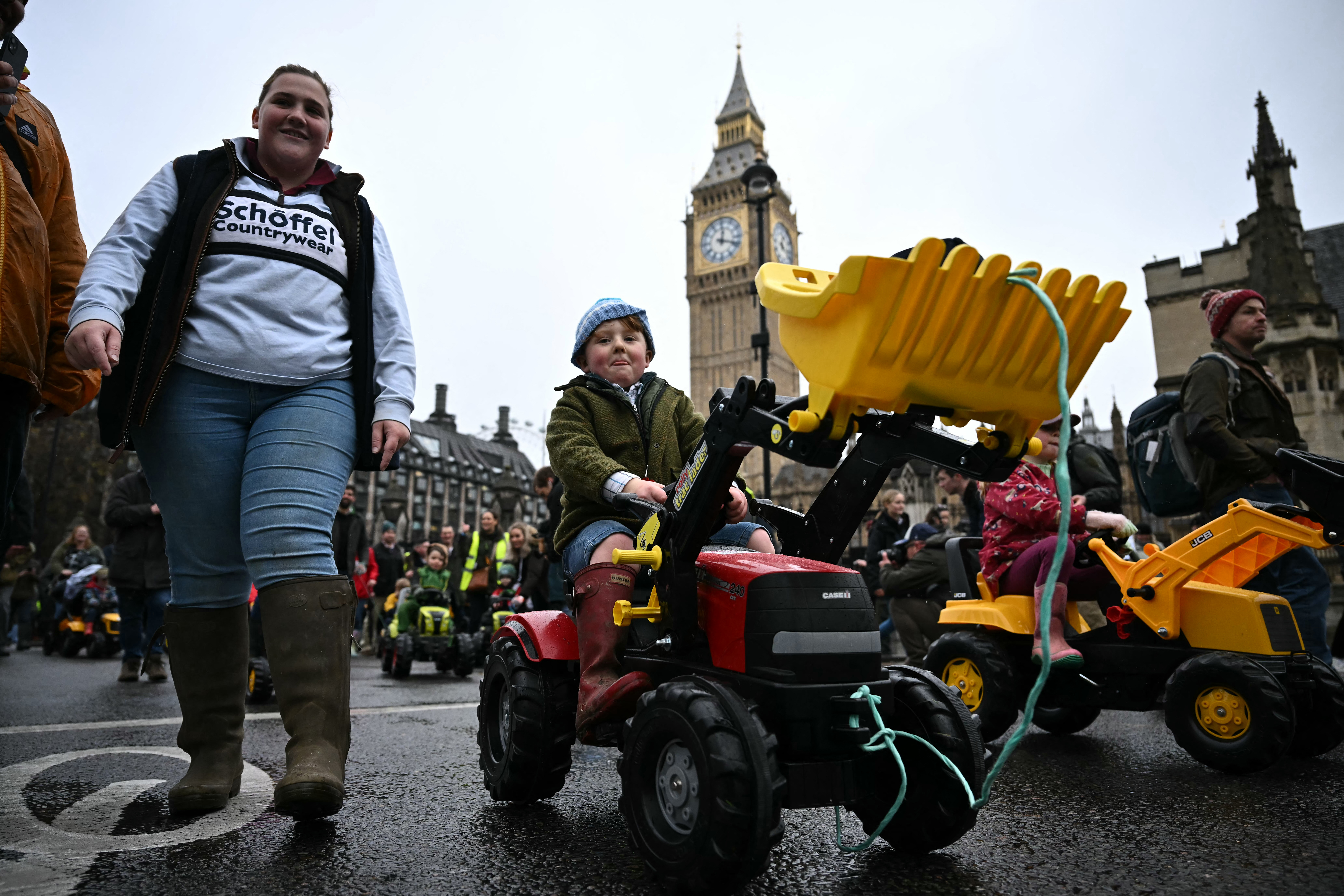 A child rides a toy tractor with a woman walking nearby