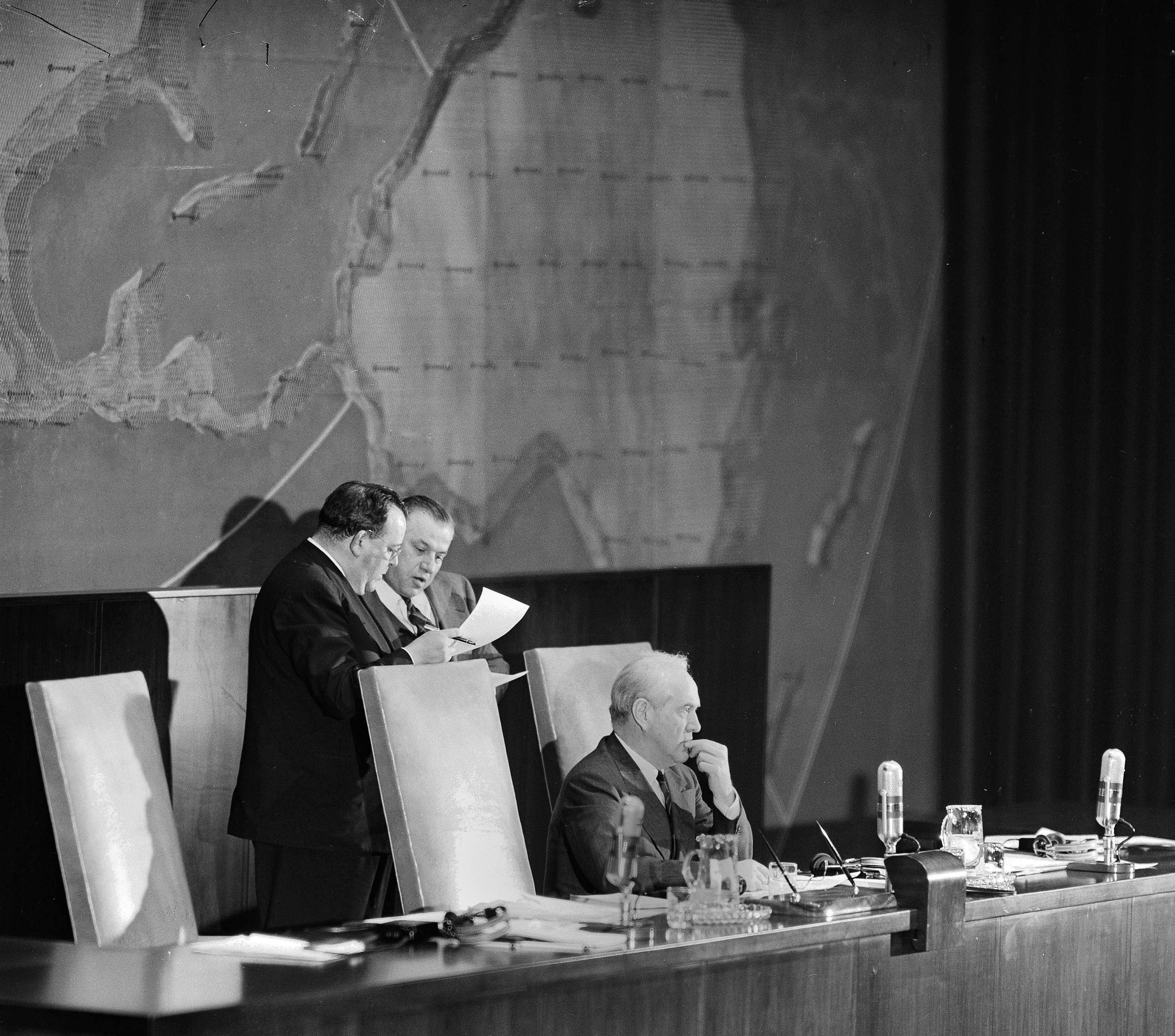 FILE - In this Nov. 29, 1947 file photo, Secretary-General Trygve Lie, left, and Andrew A. Cordier, his executive assistant, check their lists following the vote on the Palestinian partition question by the United Nations General Assembly delegates meeting at the Queens Museum in New York. Oswaldo Aranha of Brazil, president of the General Assembly, awaits their verdict on the crucial vote to set up independent Jewish and Arabic countries. The Israeli ambassador to the United Nations and the Queens Museum both say a ceremony will be held Nov. 29, 2017 on the 70th anniversary of the vote. The agreement comes after museum officials initially reneged on plans for the event. (AP Photo/Matty Zimmerman, File)
